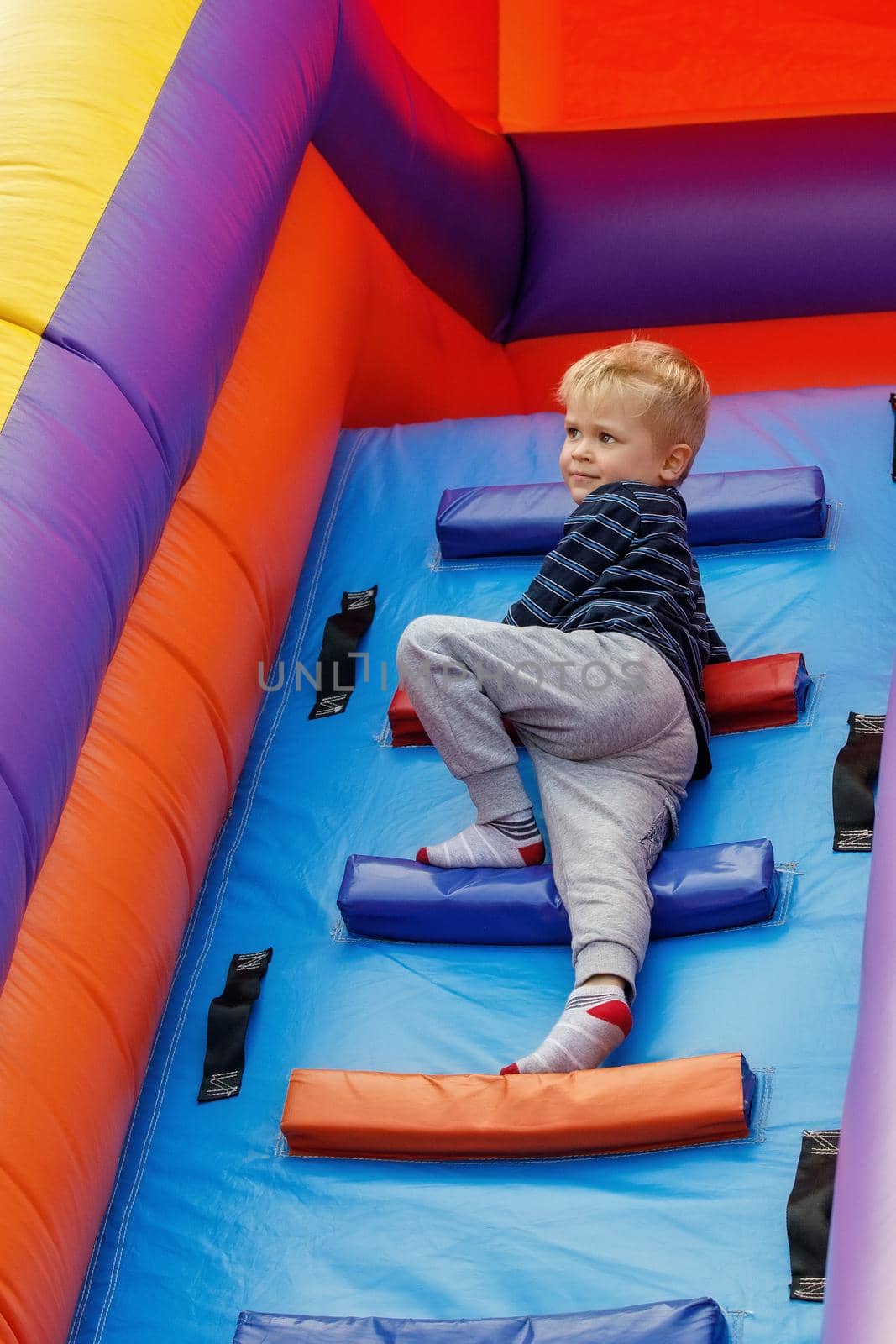 Little boy child climbs the stairs of a multi-colored slide in the park. by Lincikas