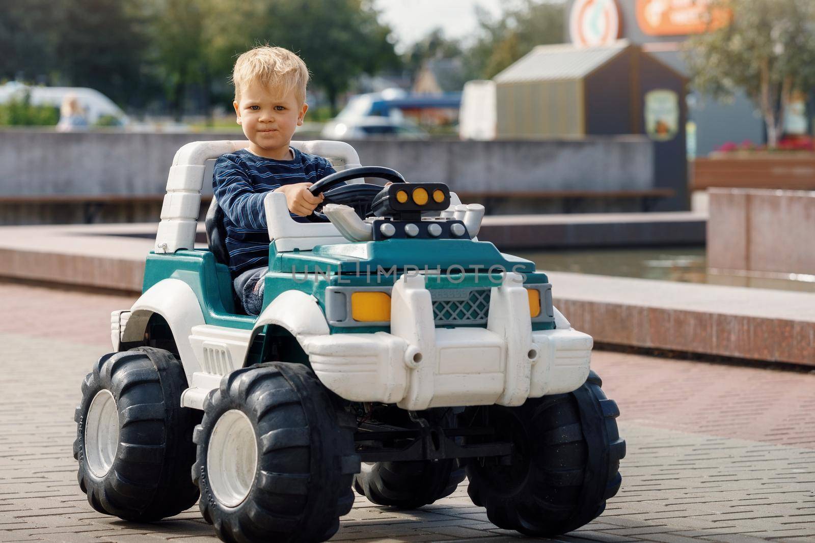 The happy blond boy is very focused, driving a big green toy SUV.