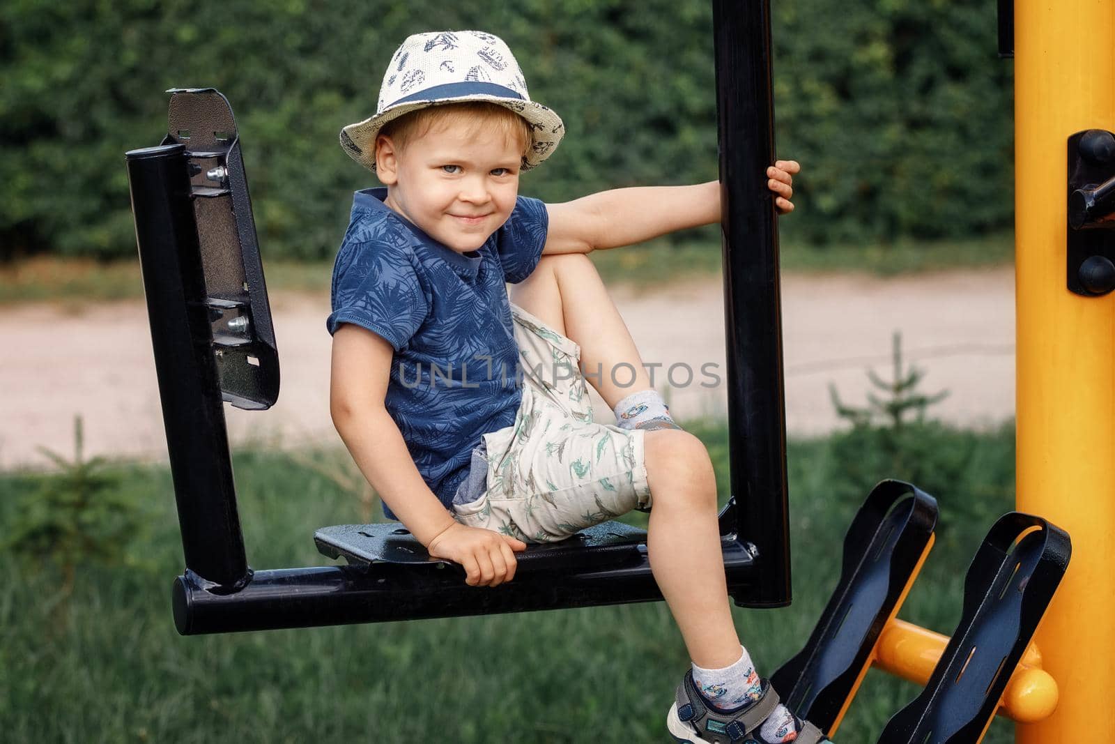 Boy child doing sports exercises on the outdoor sports ground. The child in the hat looks at the camera and smiles.