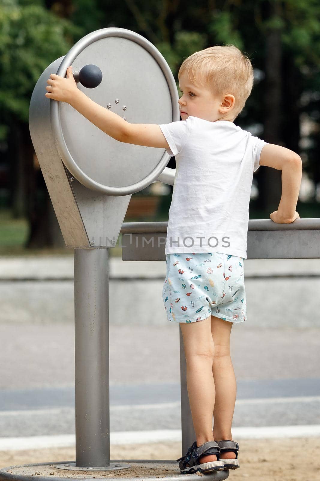 A little boy wearing shorts and a t-shirt plays with a tap in a public park.