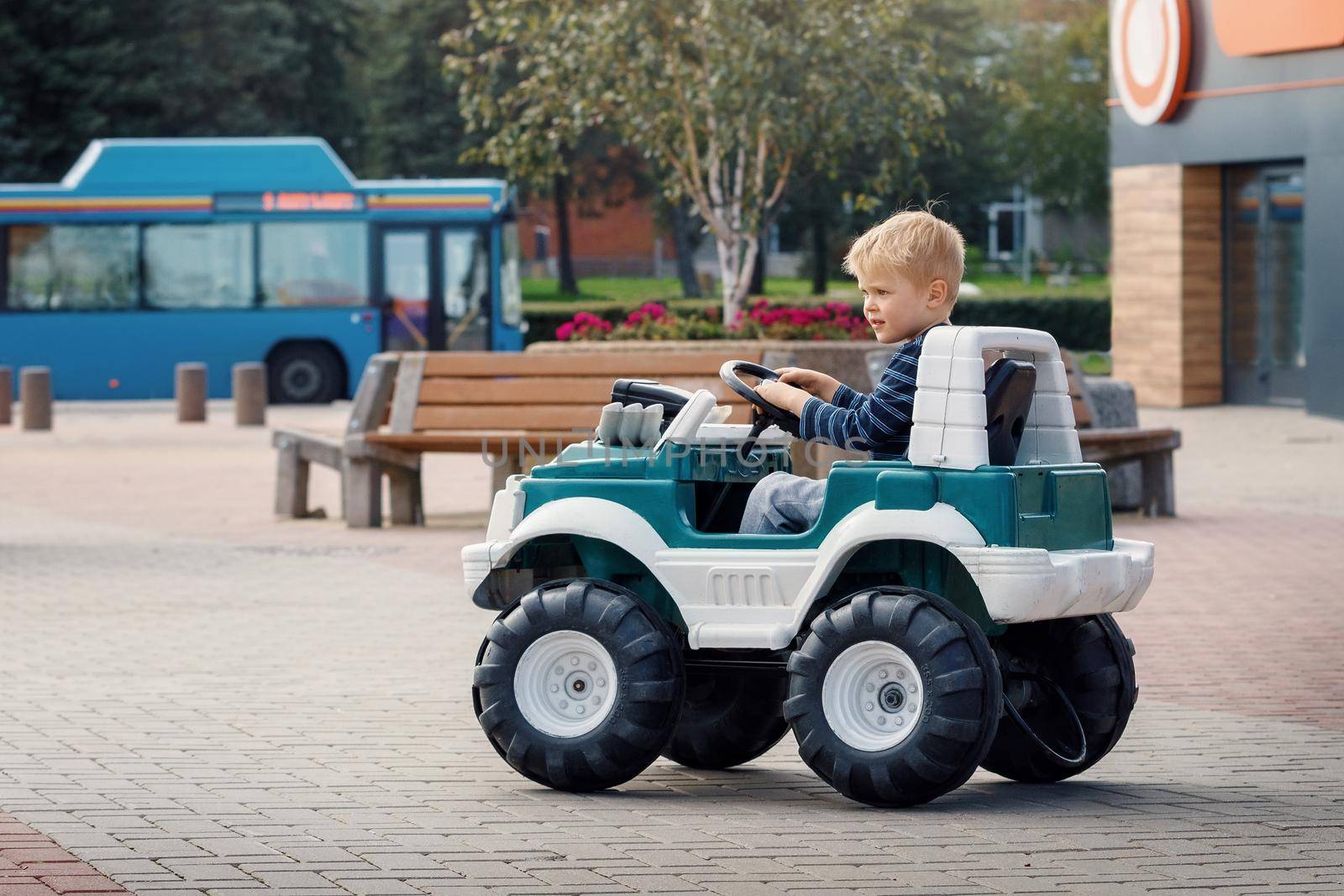 Little preschool kid boy driving big toy car and having fun outdoors. Child enjoying warm summer day in city landscape. by Lincikas