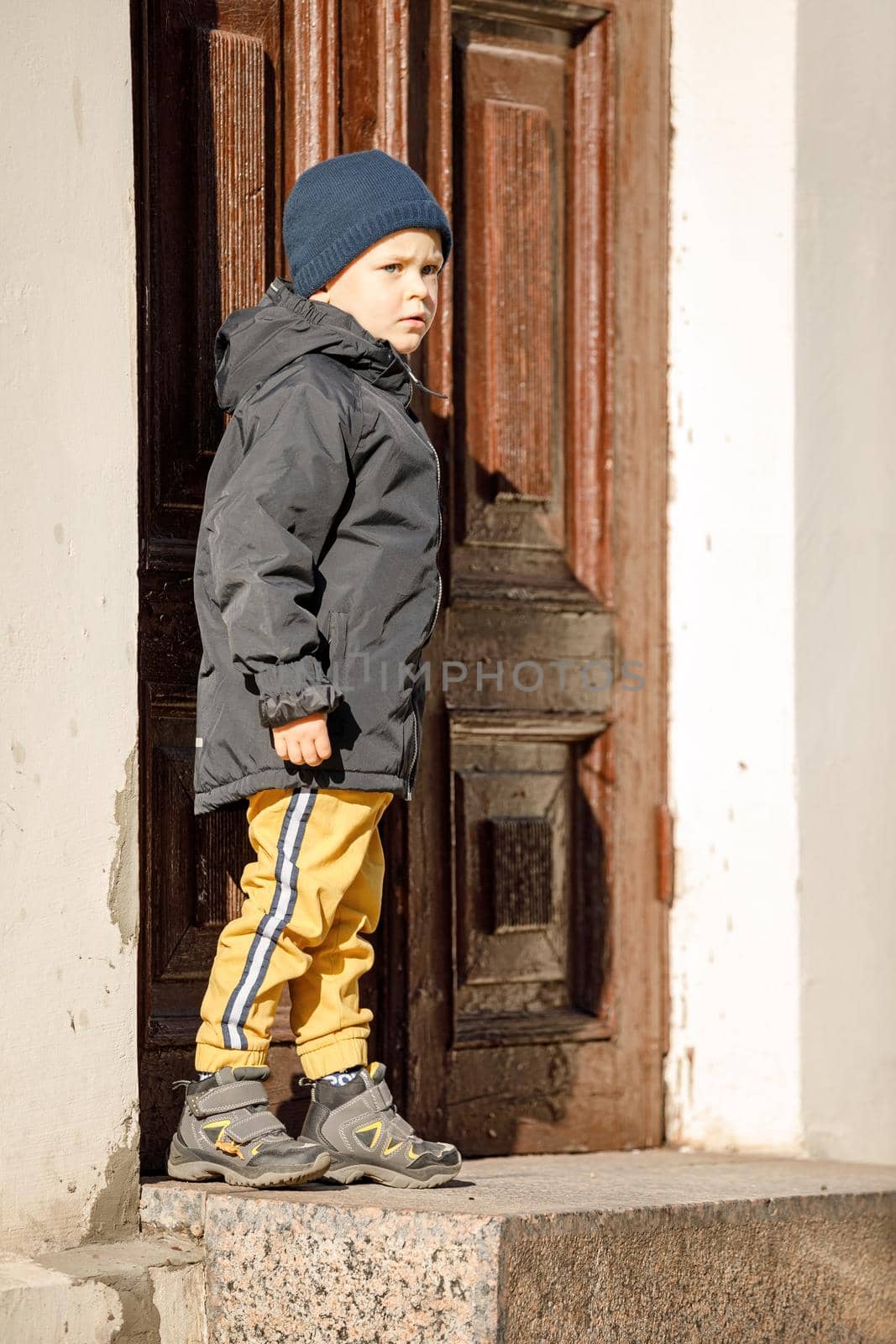 A cute boy on an autumn day at the ancient door in the center of Klaipeda Old Town by Lincikas