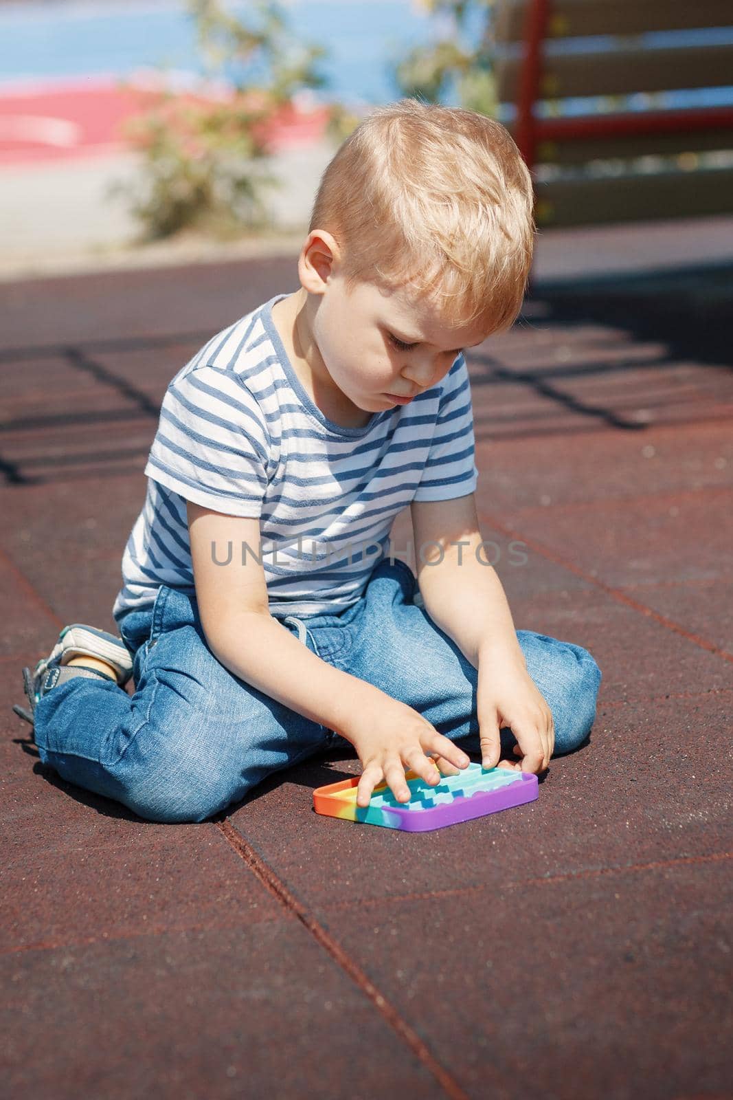 The child kneels on the floor of the playground and plays with a colorful toy for relaxation by Lincikas