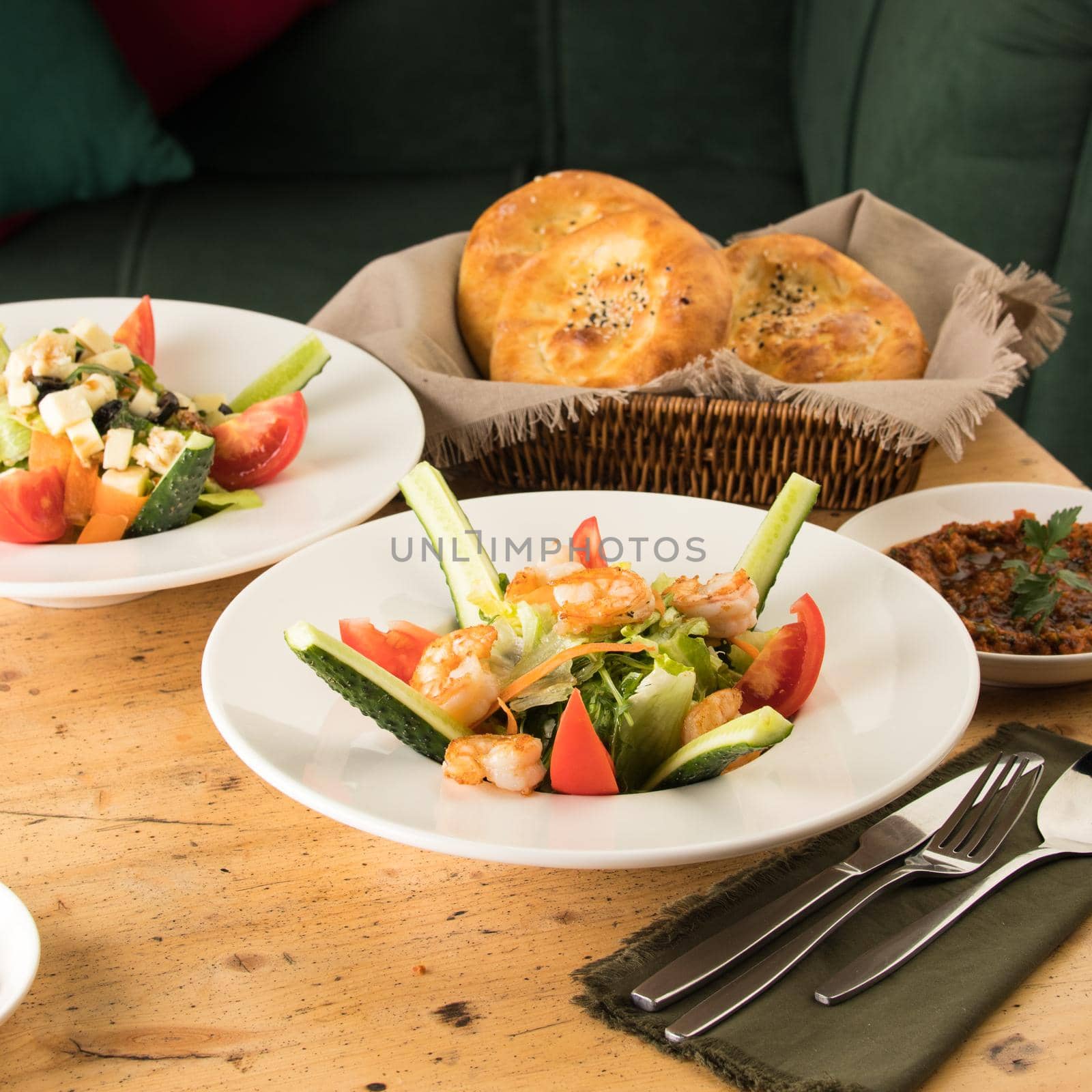 A dining table full of delicious salad on a white plate next to basket of bread