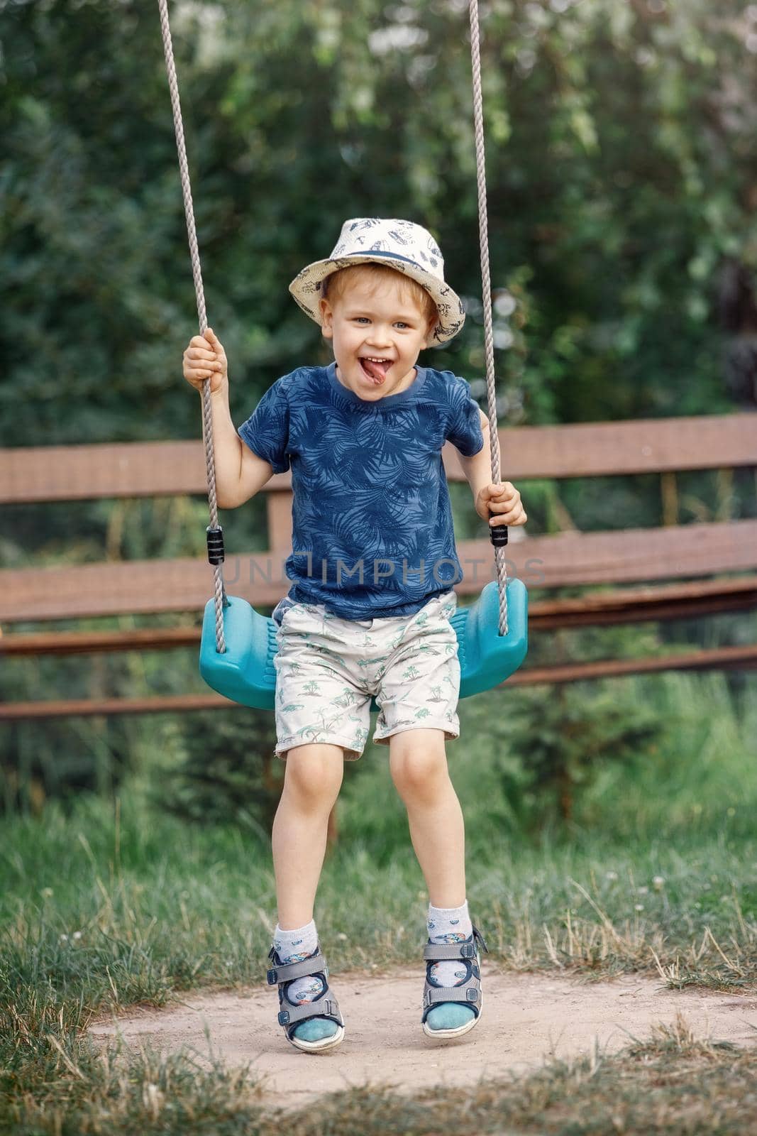 One cute little boy having fun on a swing in beautiful summer garden on warm and sunny day outdoors. Active summer leisure for kids. by Lincikas