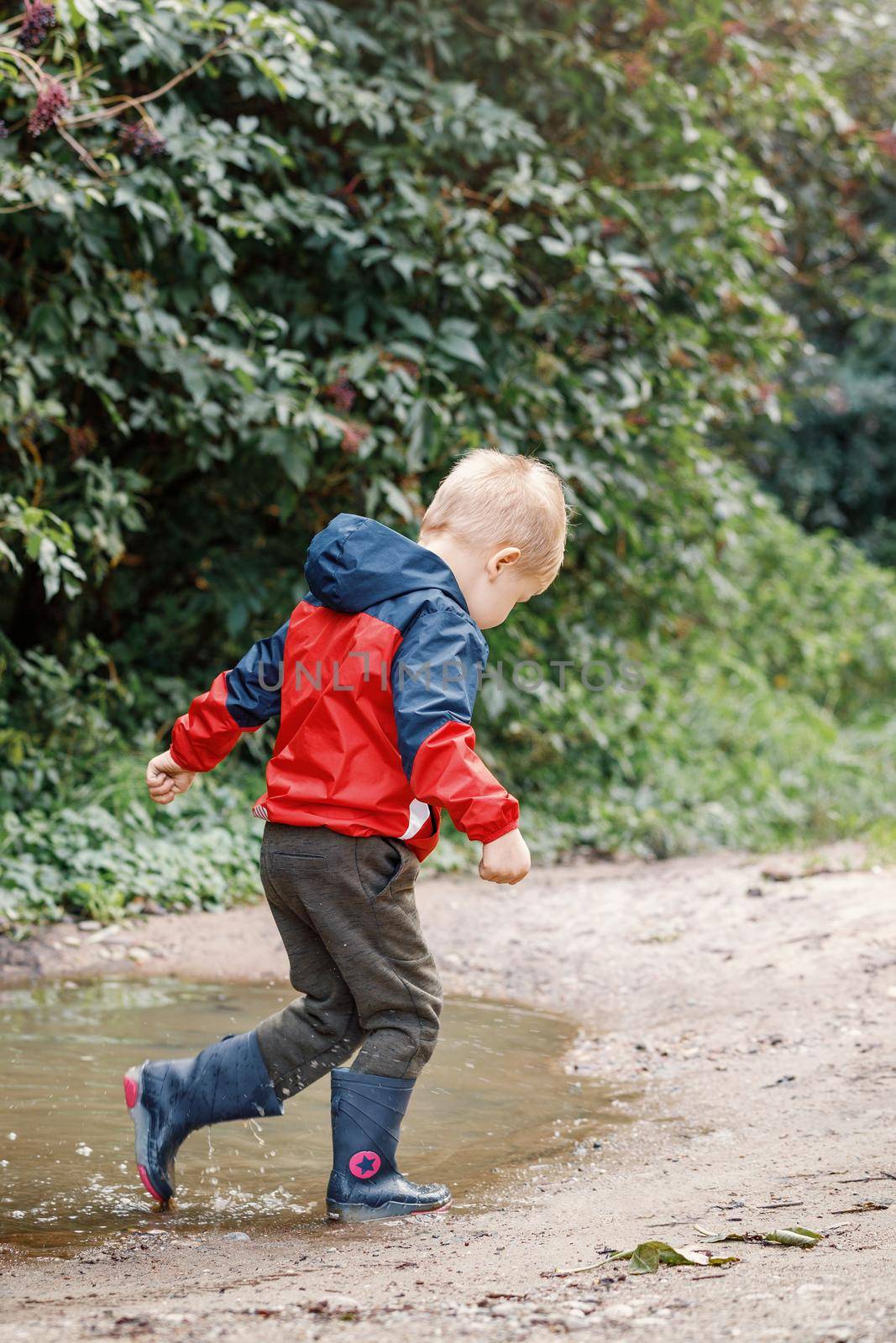 Playful boy splashing water in puddle on road.