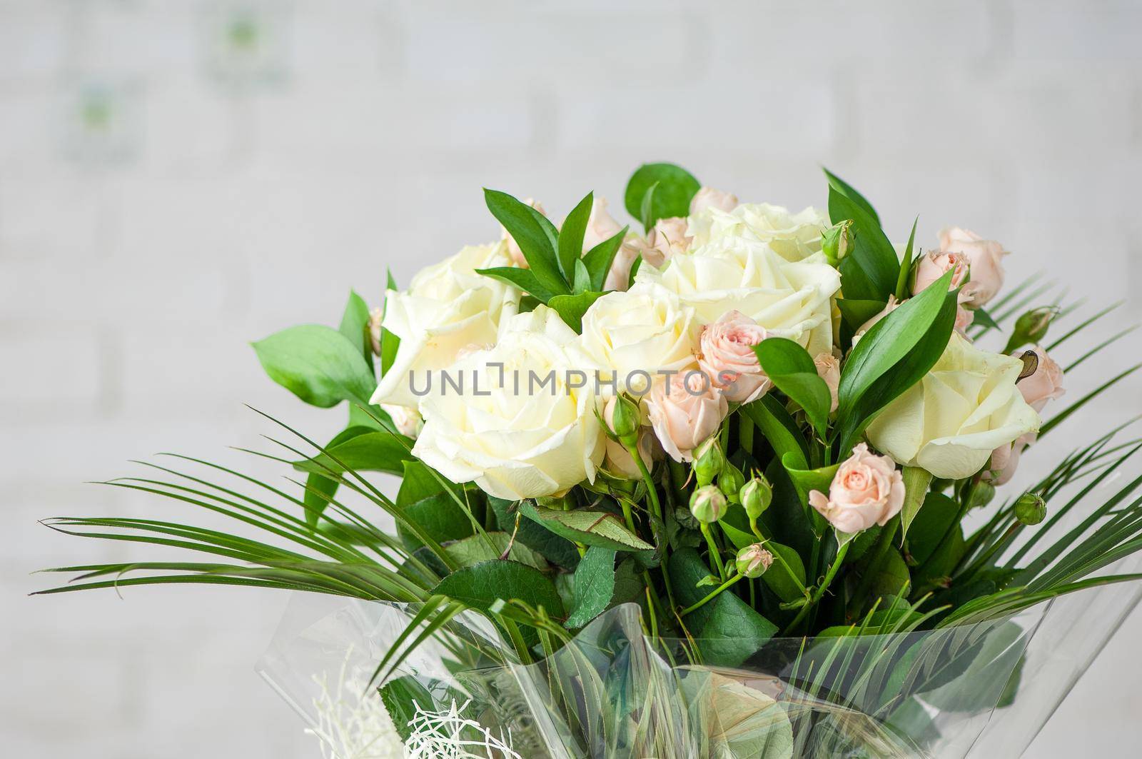 A beautiful bouquet with fresh fragrant white roses and decorative grass against a white wall