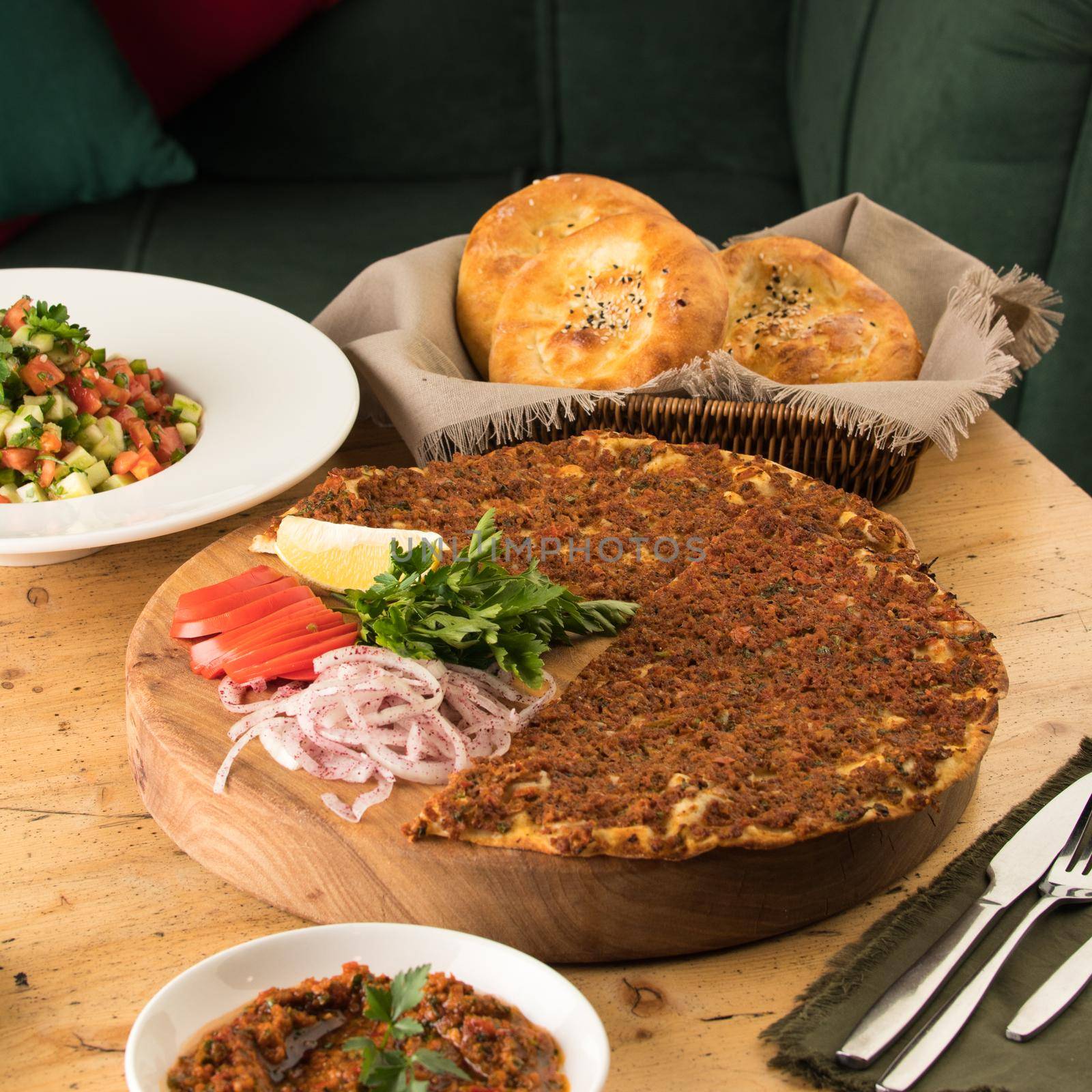 Close up shot of a lahmacun and a salad near basket of breads by A_Karim