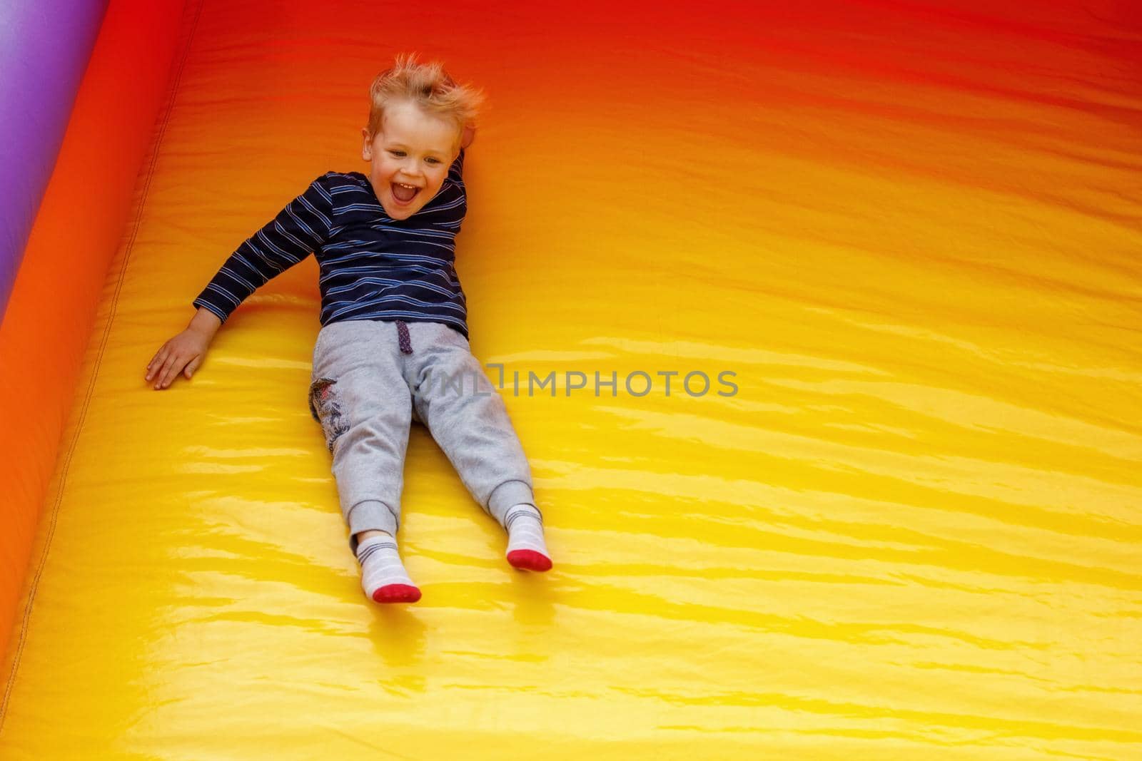 A hilarious little boy slides down at a high speed off a large, bright yellow trampoline. Child on the move, there is free space for text in the photo.