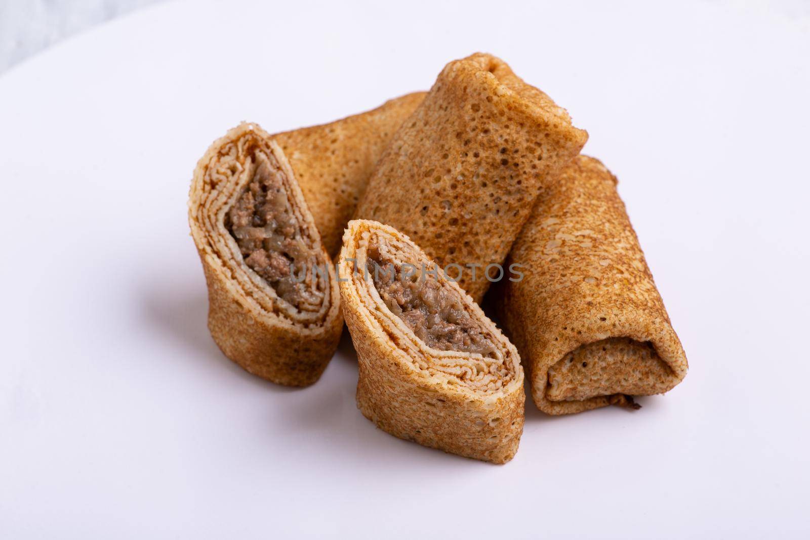 A closeup shot of stuffed pancakes with meat on a white background