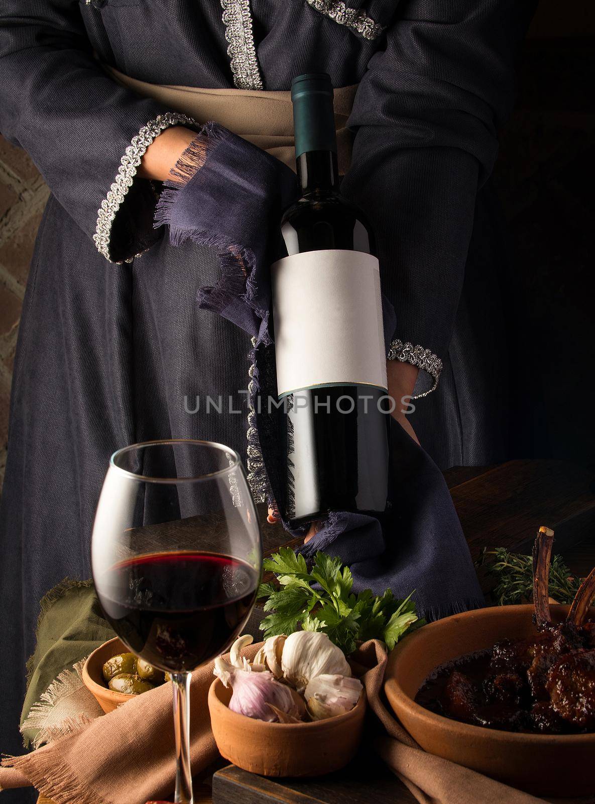 A vertical shot of a person in a traditional costume showing a wine bottle