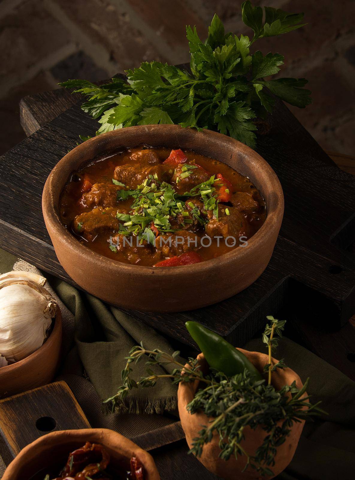 A close up shot of a meat stew and herbs in the background