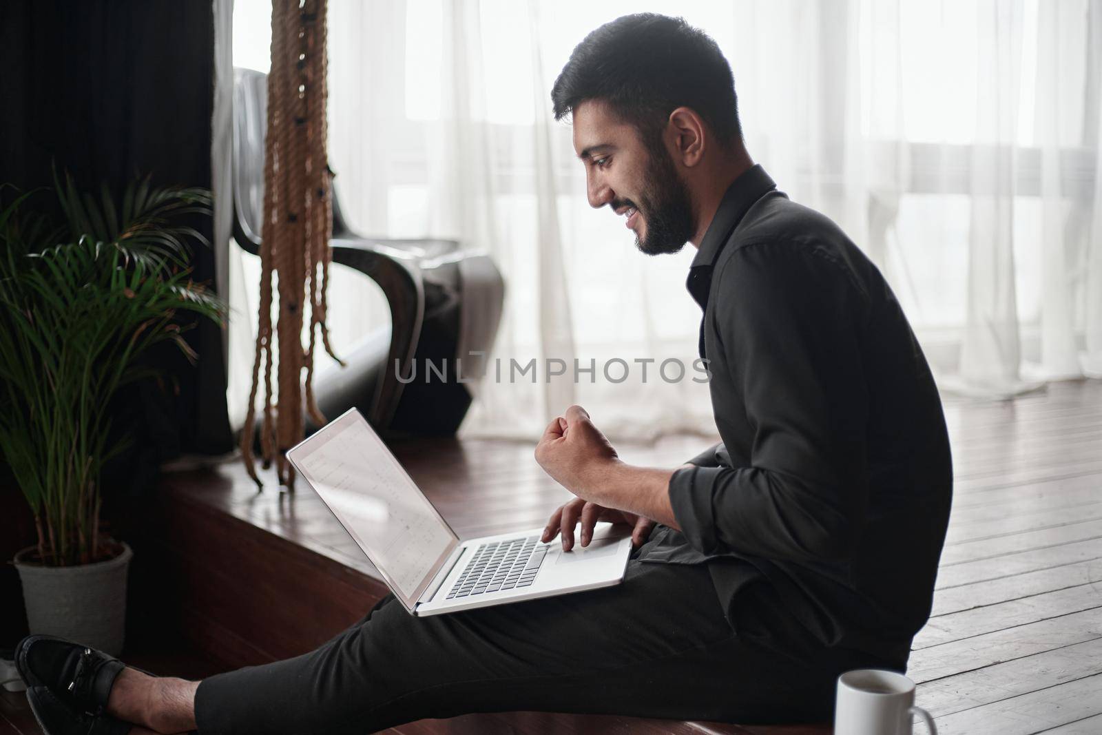 happy entrepreneur with a laptop sitting on the floor in his new store. by SmartPhotoLab