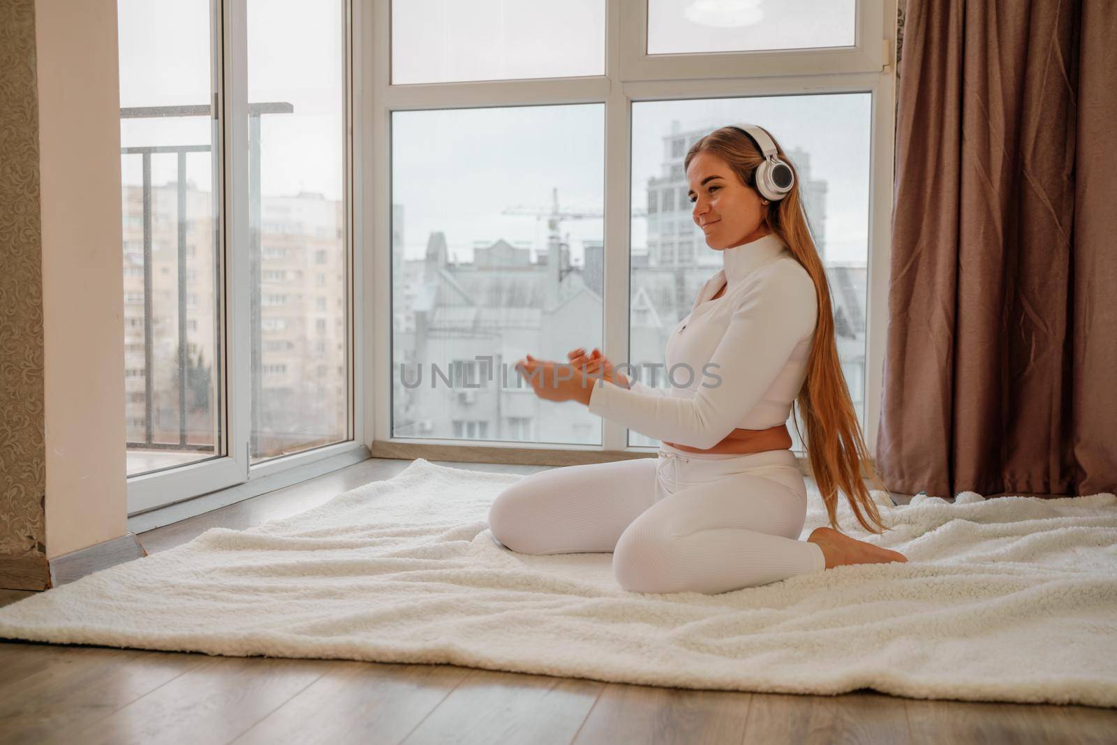 Side view portrait of relaxed woman listening to music with headphones lying on carpet at home. She is dressed in a white tracksuit