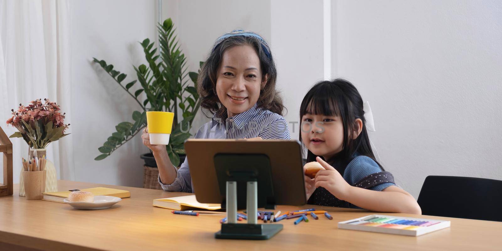 Asian grandmother and granddaughter happily pencil drawing at home.