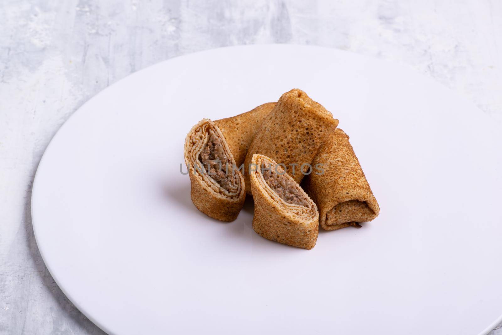 A plate of stuffed pancakes with meat on a white table