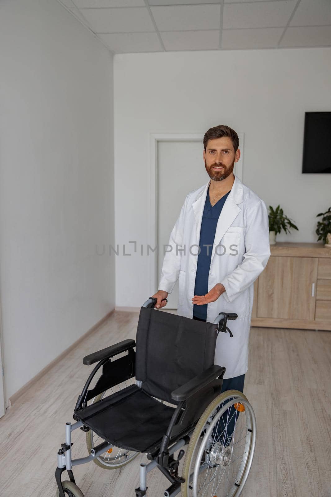 Professional doctor in uniform with wheelchair standing in the hospital ward in clinic by Yaroslav_astakhov