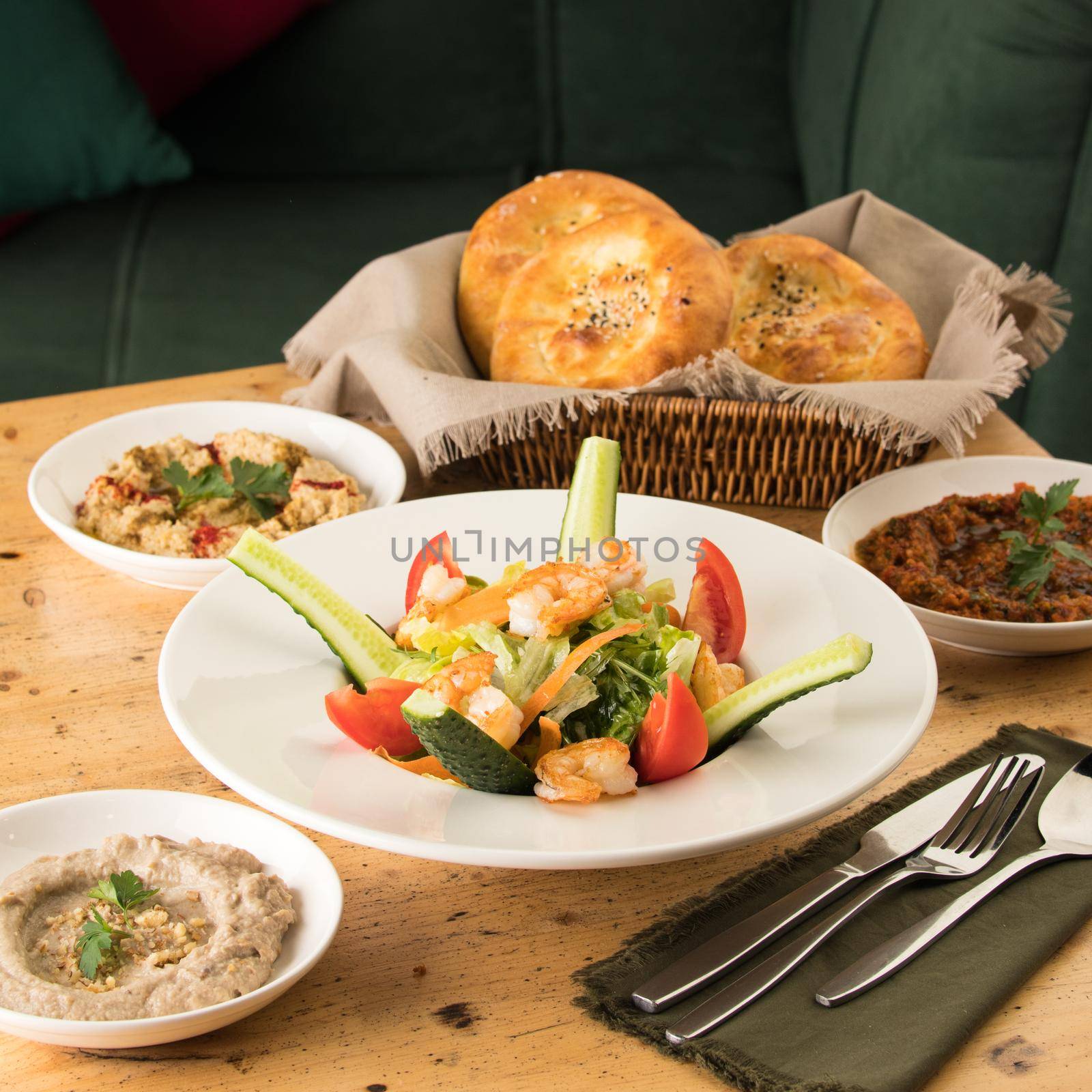 A dining table full of delicious salad on a white plate next to basket of bread