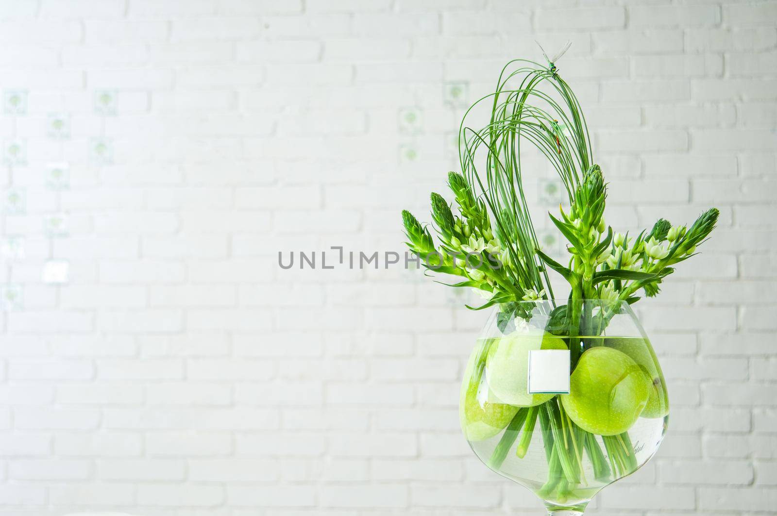 Closeup shot of Ornithogalum plant and apples in a large glass cup on a table by A_Karim