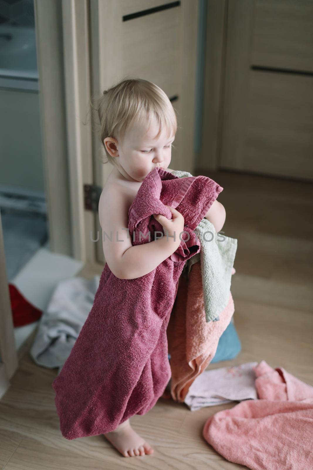 cute funny baby playing with stack of towels in the bathroom at home by paralisart