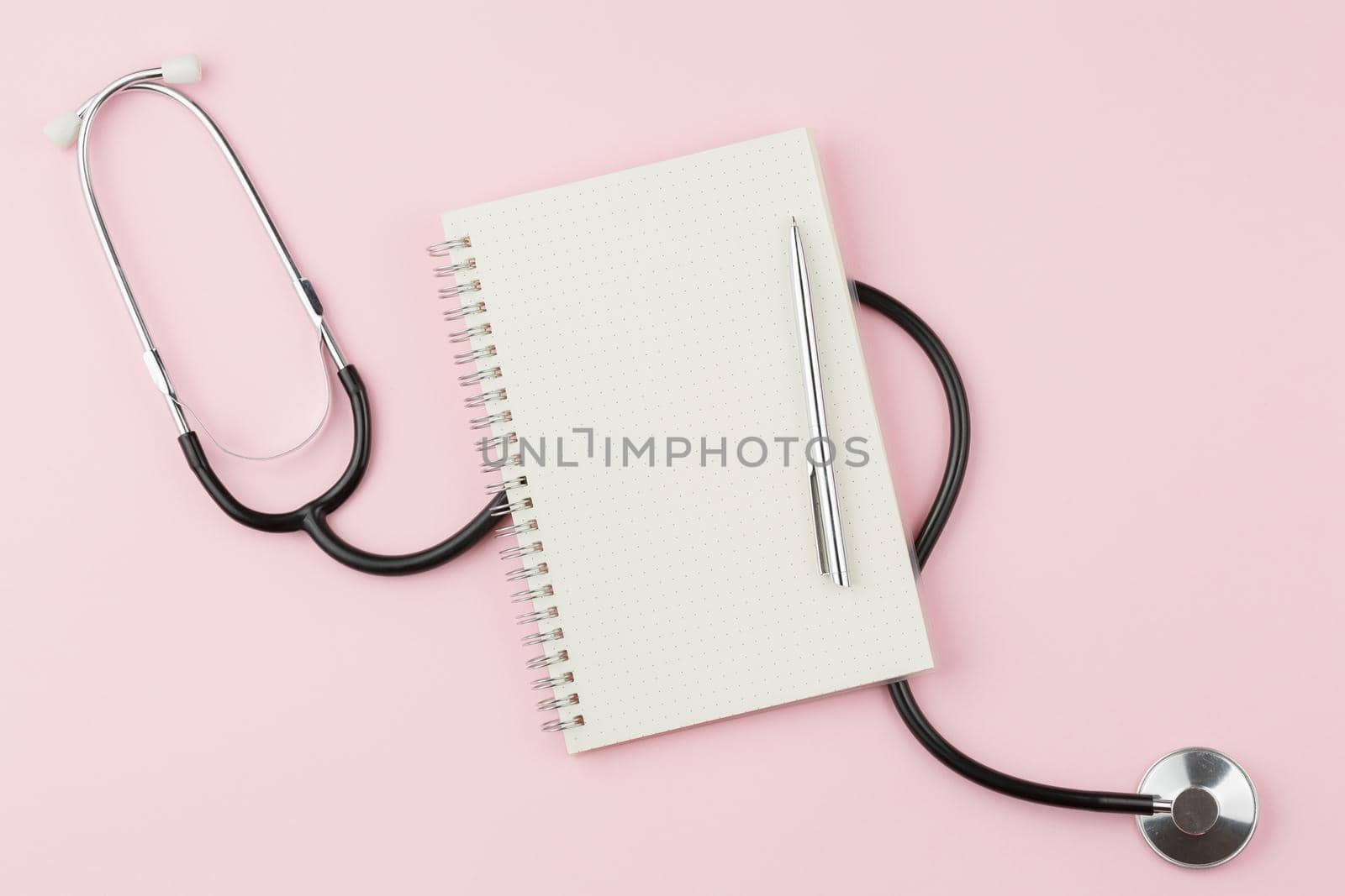 Spiral notepad with a pen on a pink background. Top view. The stethoscope is on the doctor desk. Flat lay.