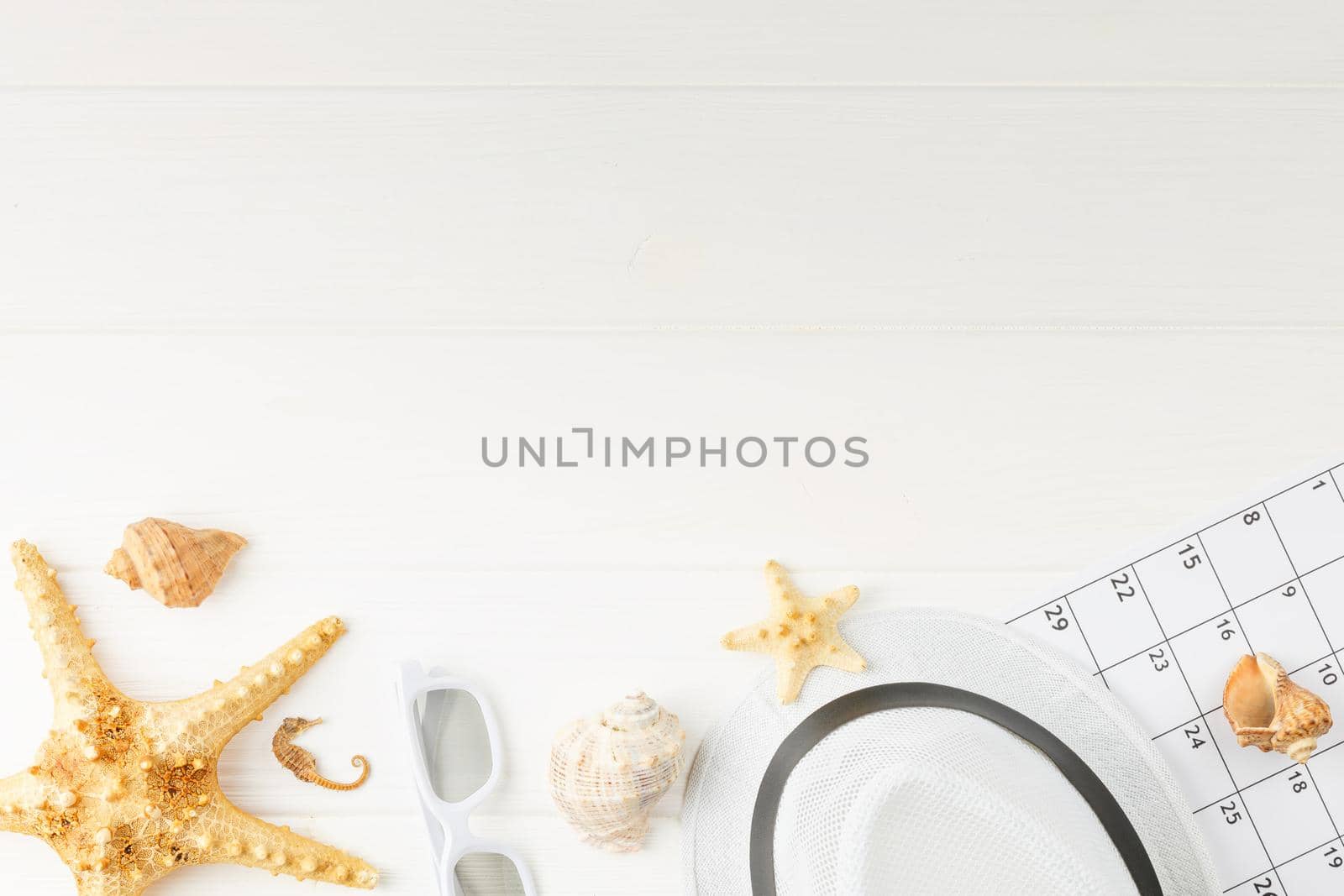 Vacation calendar at the sea on white wooden background. Summer holiday concept. Decoration of starfish and seashells. Top view. Banner with corals and seahorses. Beach hat with sunglasses.