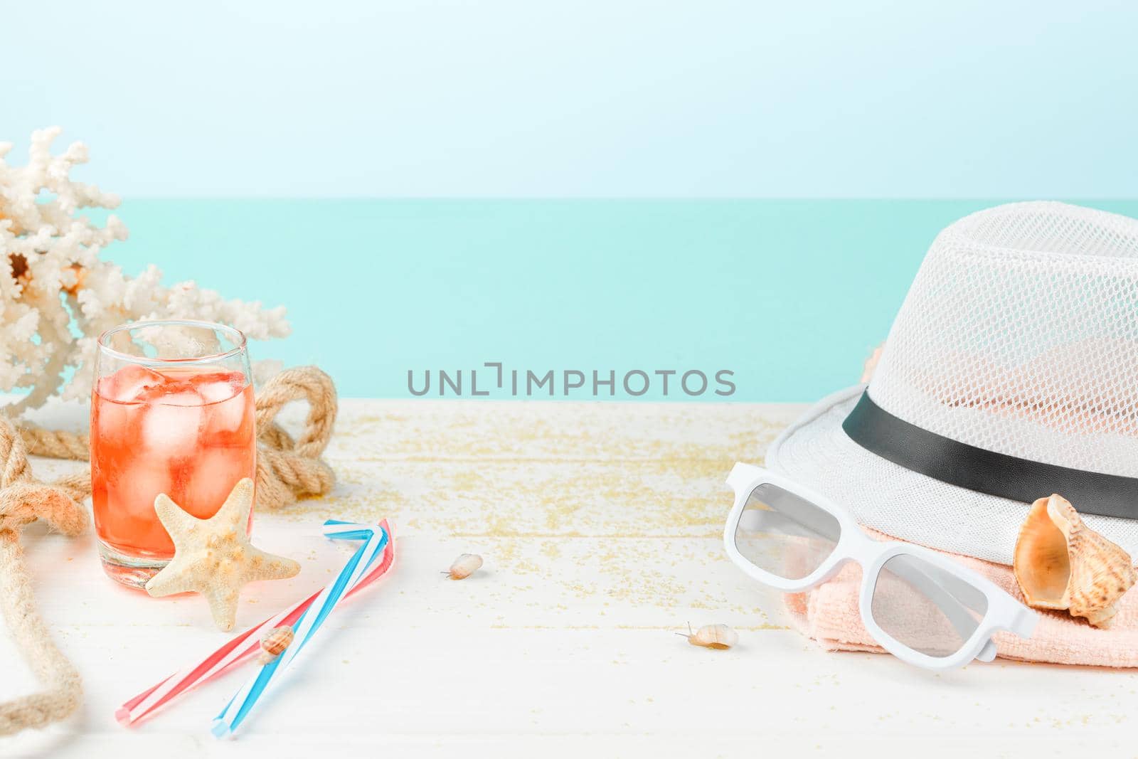 Summertime relax. Summer accessories on a white wooden table. Sea vacation concept. Cocktail with ice and red raspberries. Seashells with corals and snails.