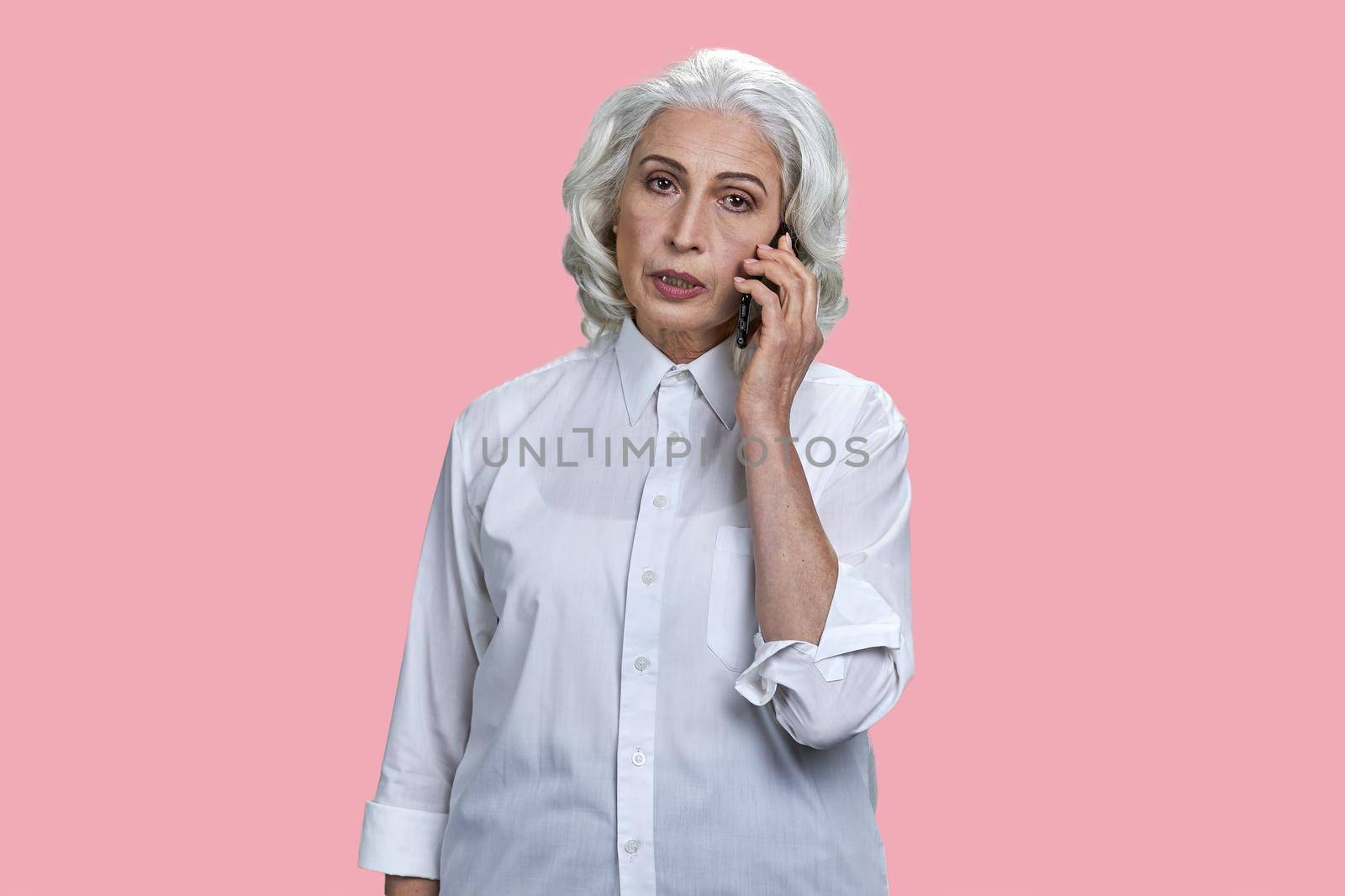 Portrait of elegant senior woman talking on mobile phone. Beautiful gray haired woman talking on cell phone on pink color background.