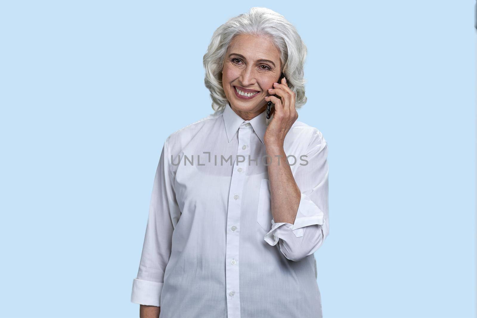 Happy senior business woman talking on mobile phone. Light blue background.