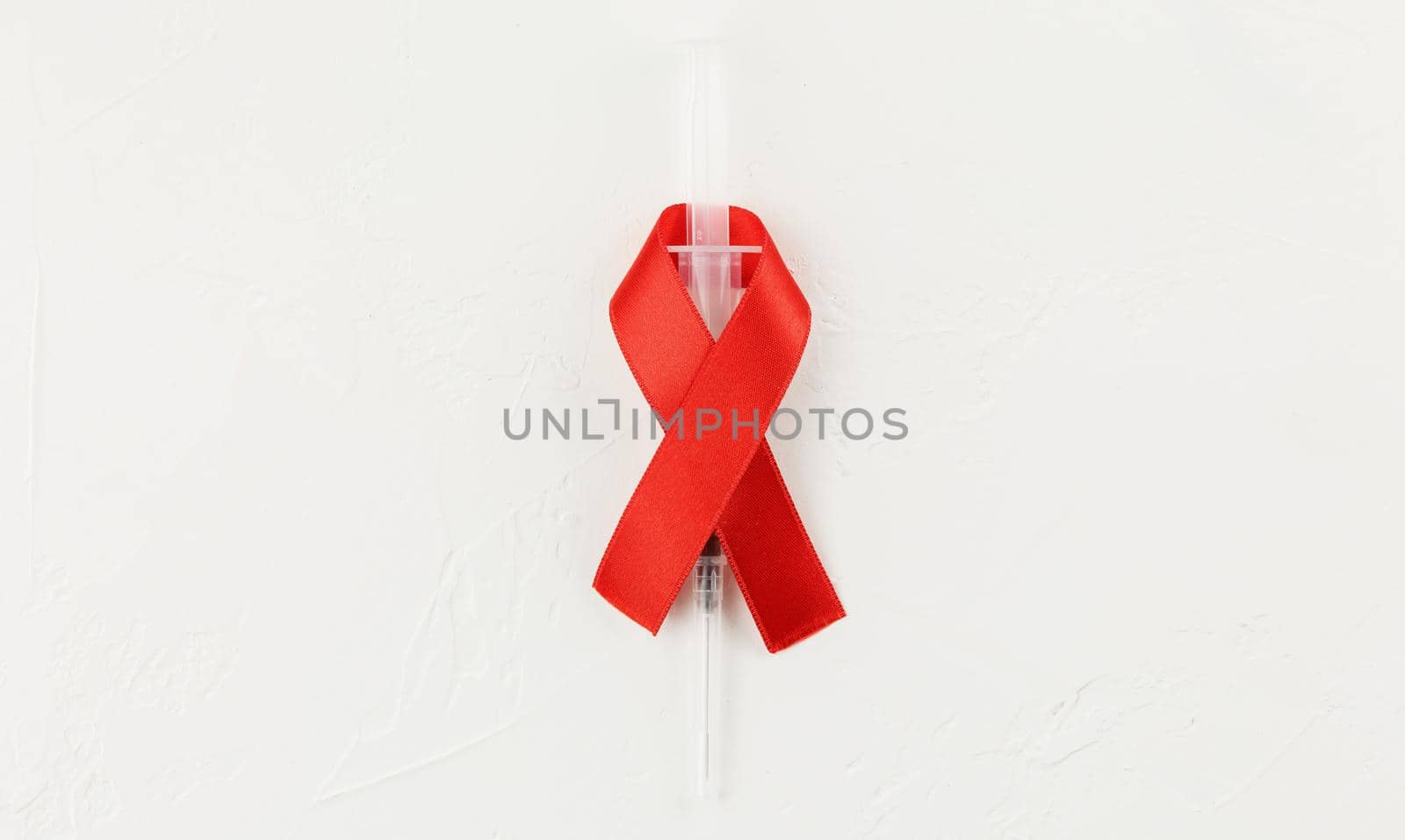 Red ribbon with vacutainer on a white grunge background. Top view. Health care. AIDS prevention concept. Hiv and cancer awareness. Test tube container. Flat lay.