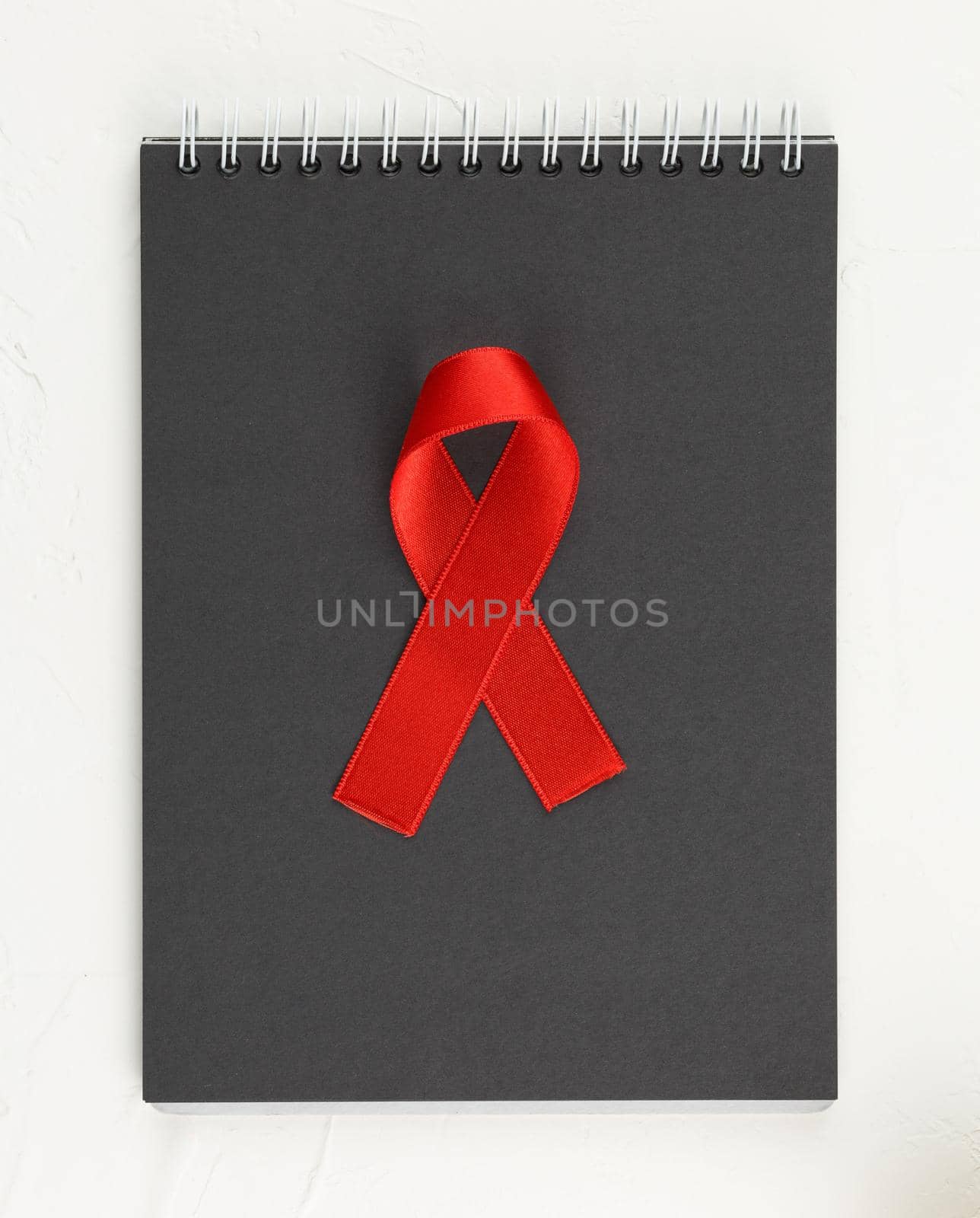 Red ribbon with black notebook on white grunge background. Top view. Health care. AIDS prevention concept. Hiv and cancer awareness. Flat lay.