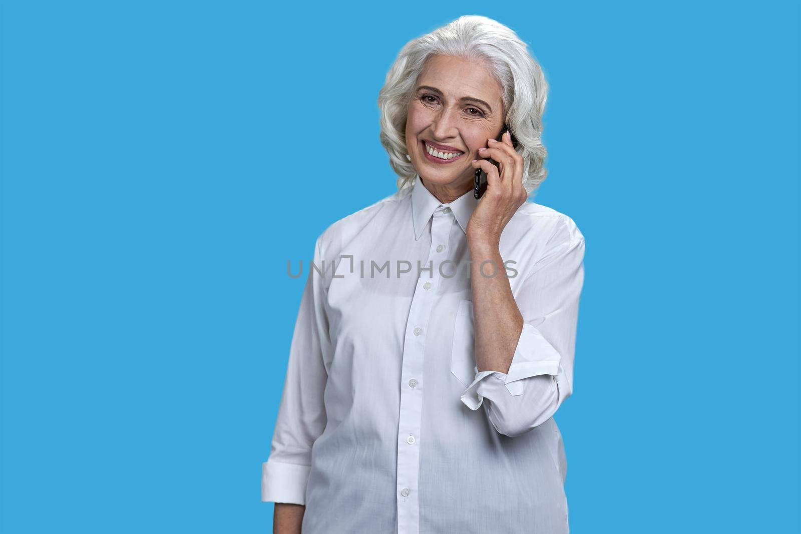 Portrait of cheerful mature business lady talking on mobile phone. Smiling senior woman talking on cell phone on blue background.