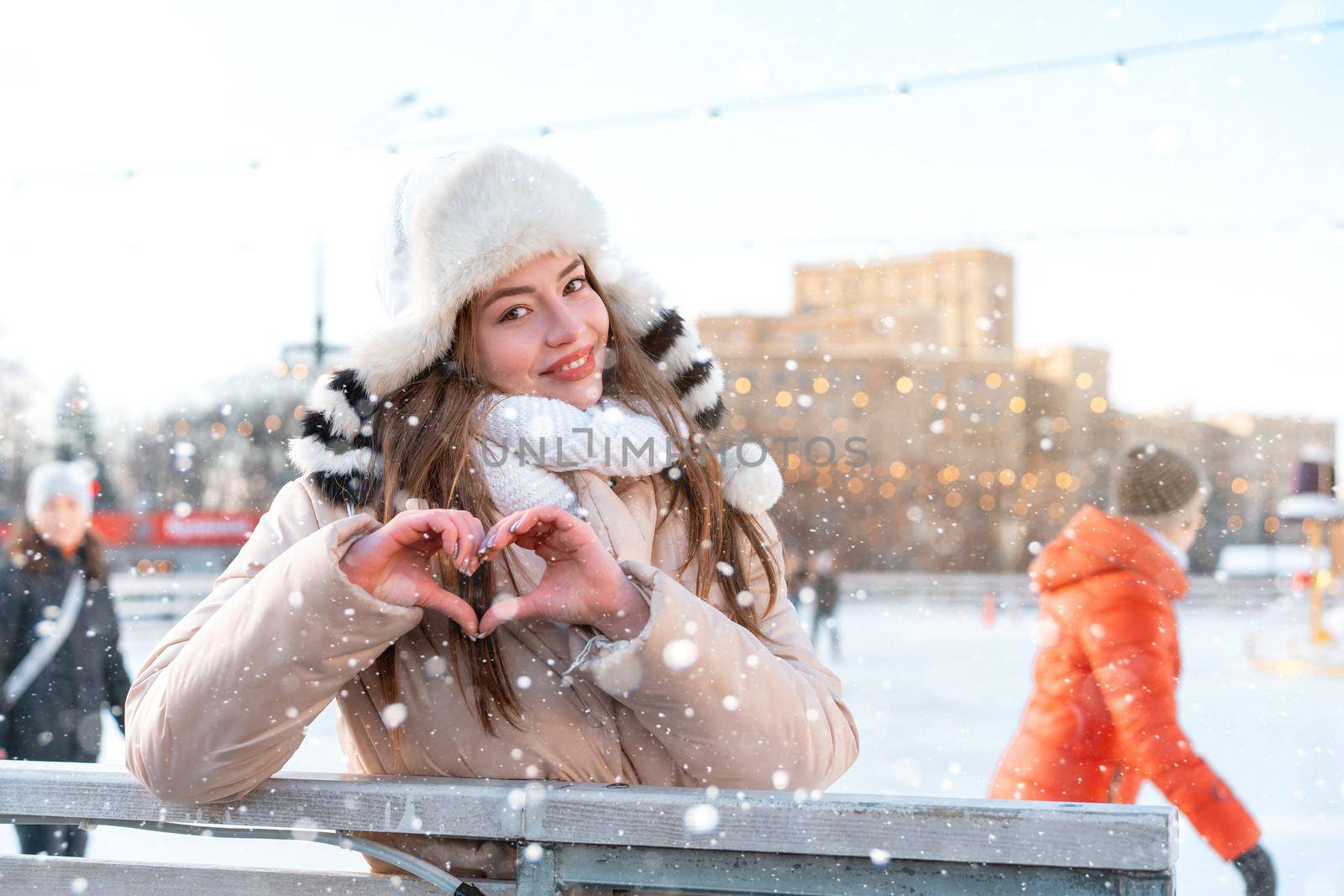 Beautiful lovely young woman long hair warm winter jackets funny fluffy hat showing heart shape by fingers. love concept Christmas mood lifestyle Happy holiday woman walk snowy day Winter leisure