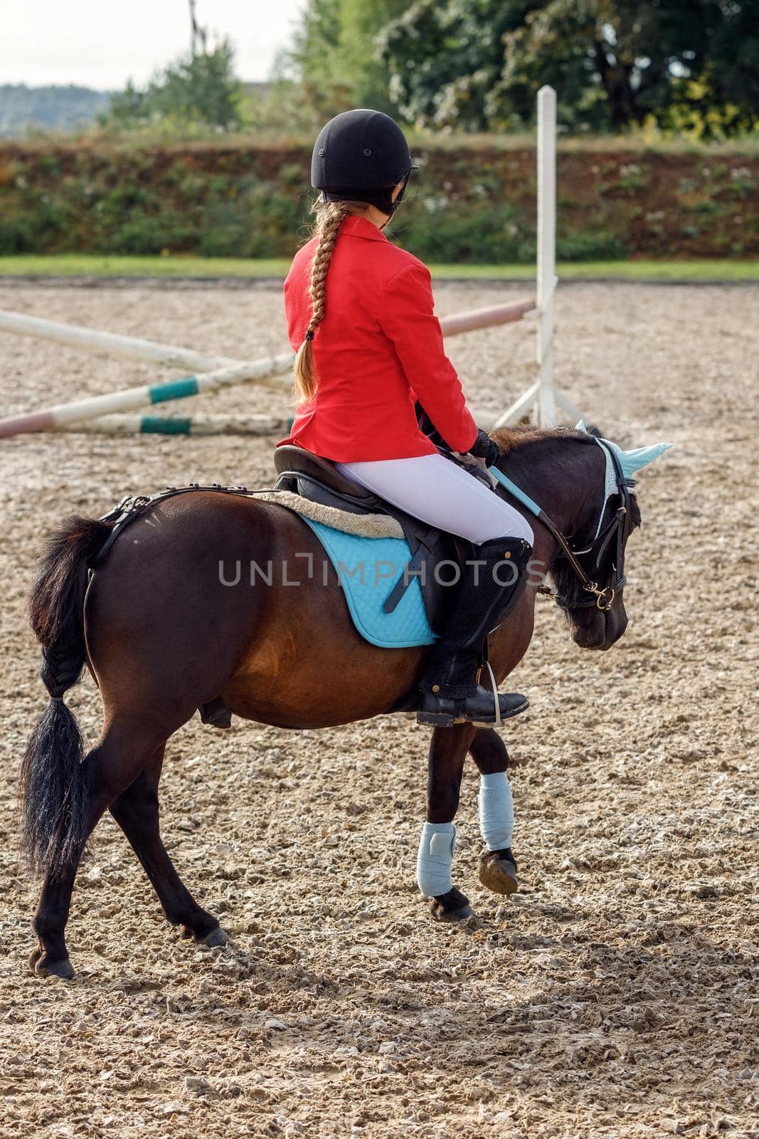 Girl in red riding clothing riding on pony over small jumps.