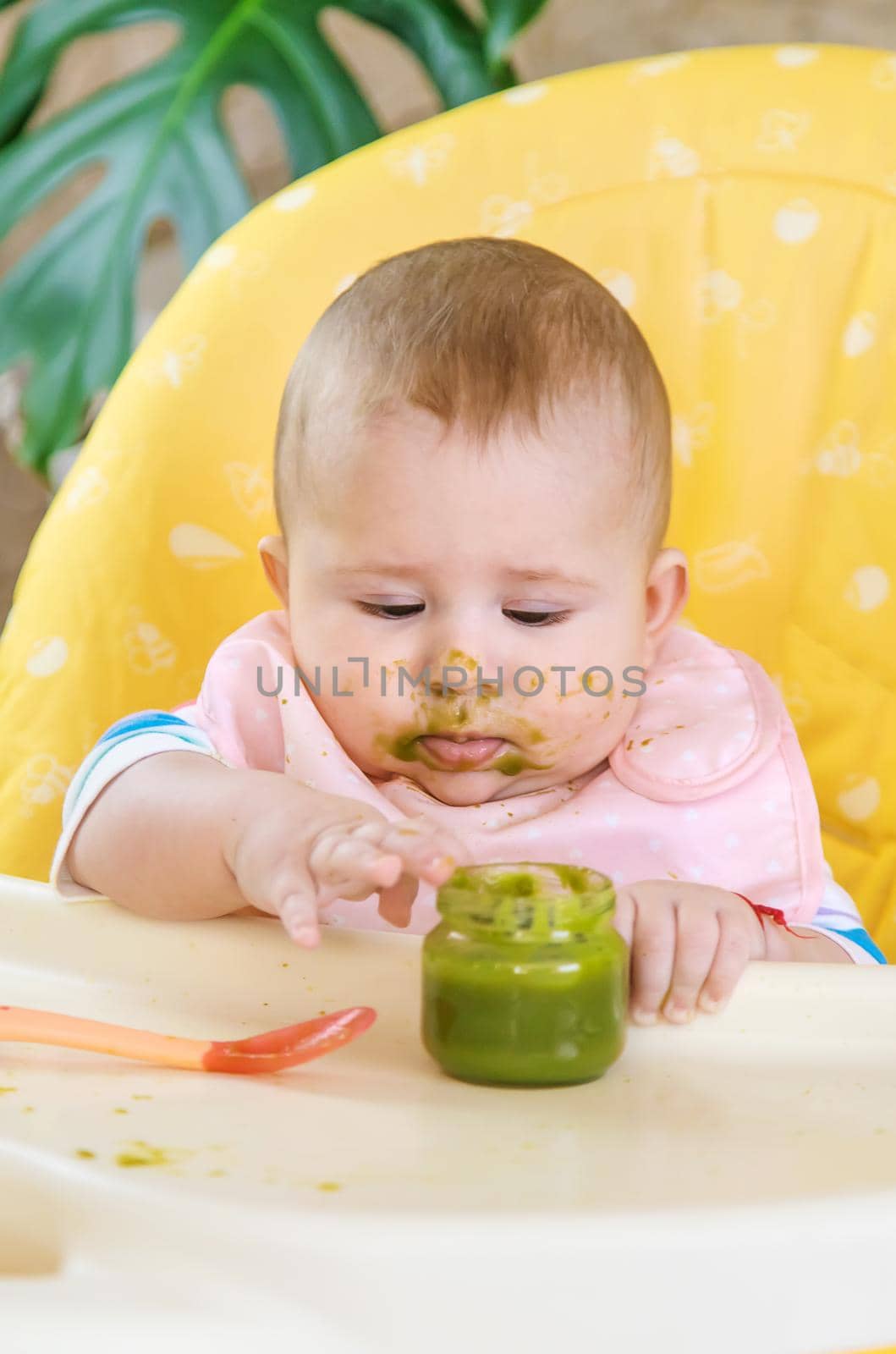 Little baby is eating broccoli vegetable puree. Selective focus. People.