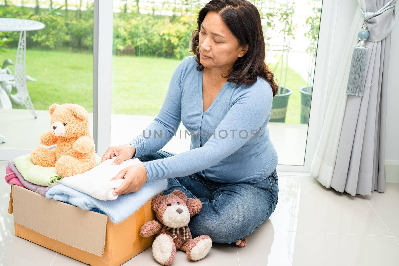 Holding clothing donation box with used clothes and doll at home to support help for poor people in the world.