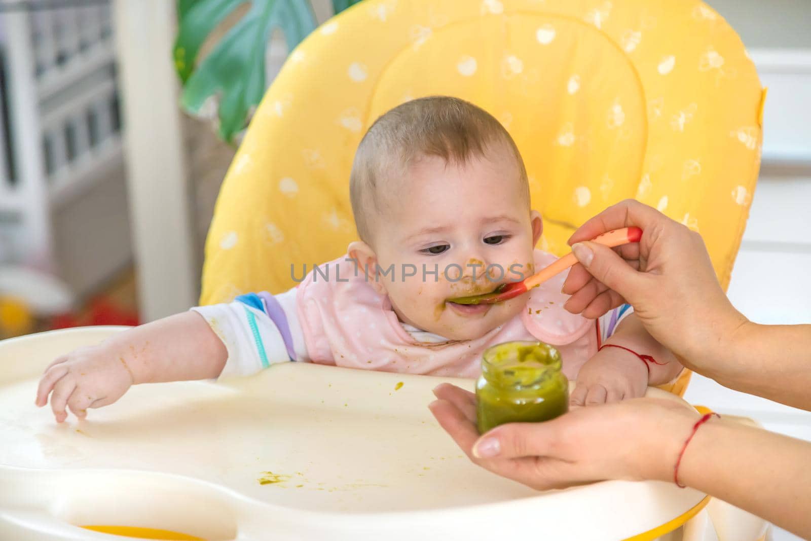 Little baby is eating broccoli vegetable puree. Selective focus. People.