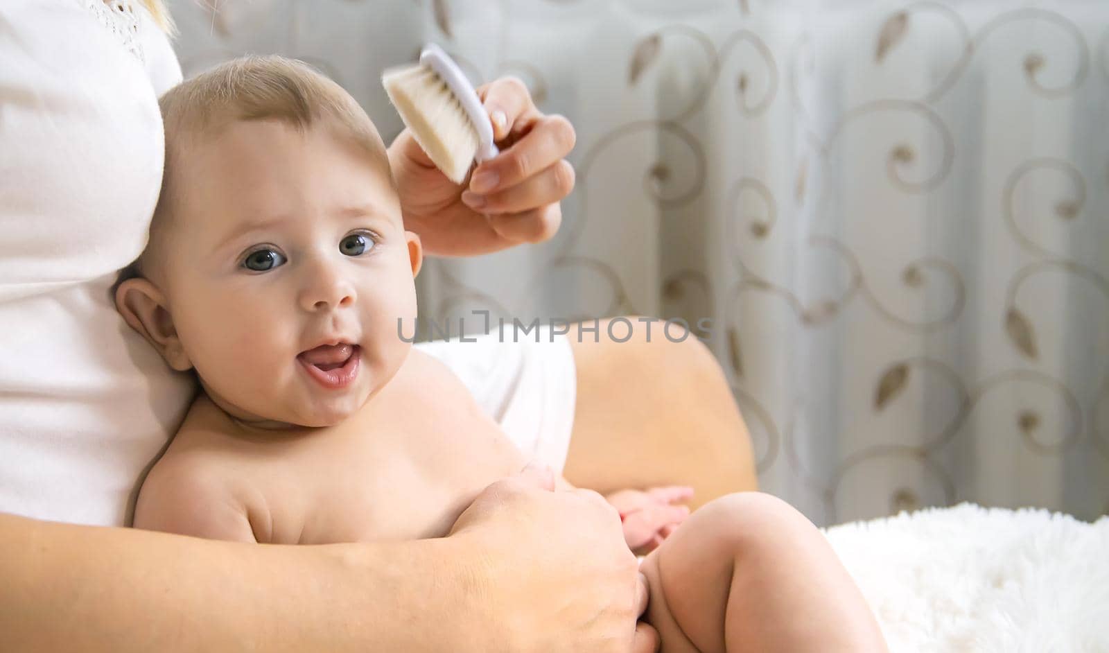 The mother is combing the little baby's hair. Selective focus. People.
