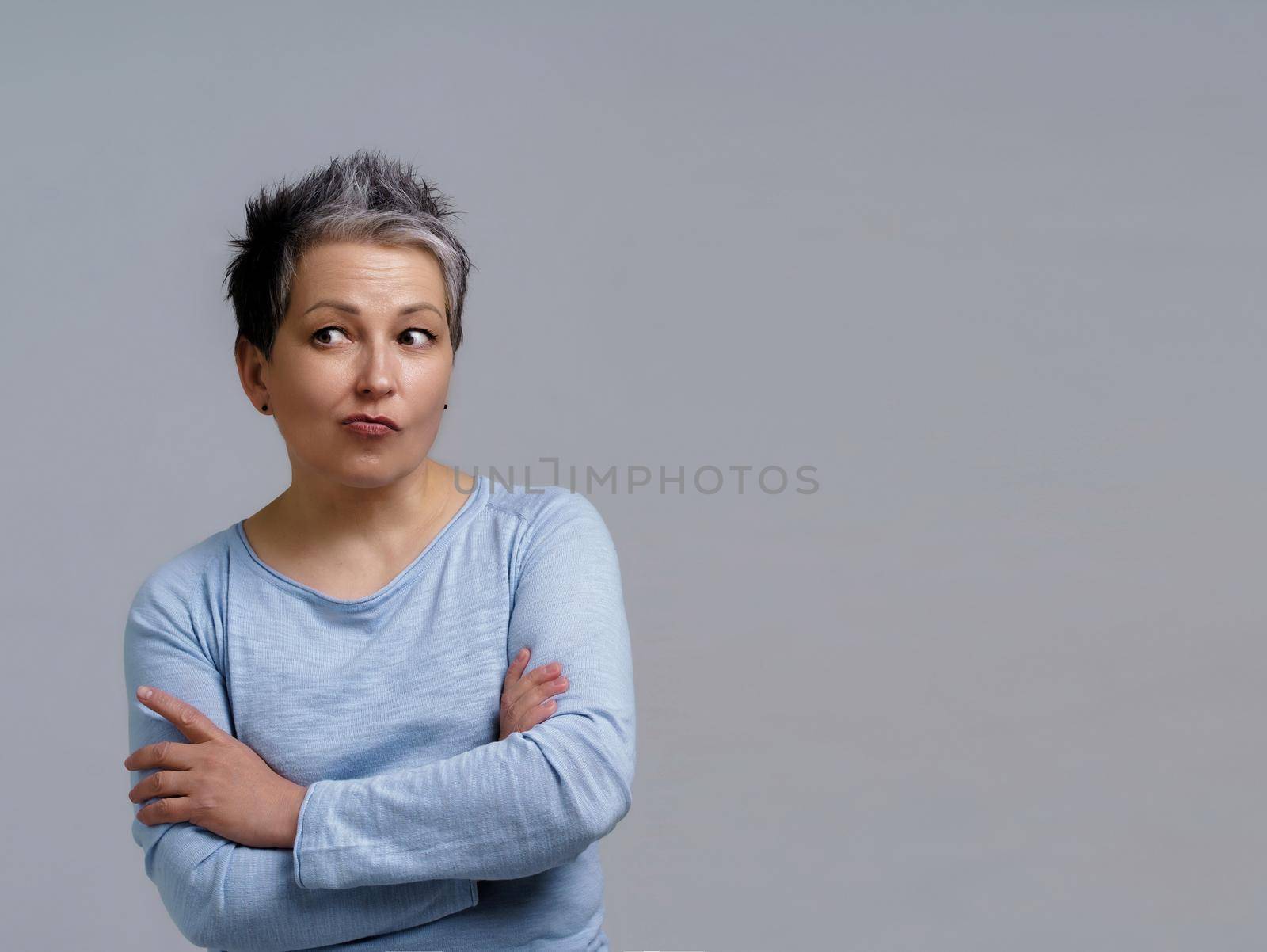 Portrait of pensive, thoughtful mature business woman with grey hair in 50s with hands folded and copy space on right for product placement isolated on white background by LipikStockMedia