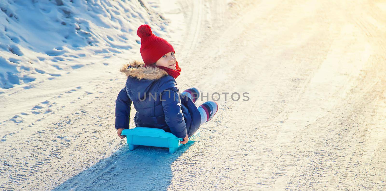 A child girl slides down a hill in the snow. Selective focus. People.