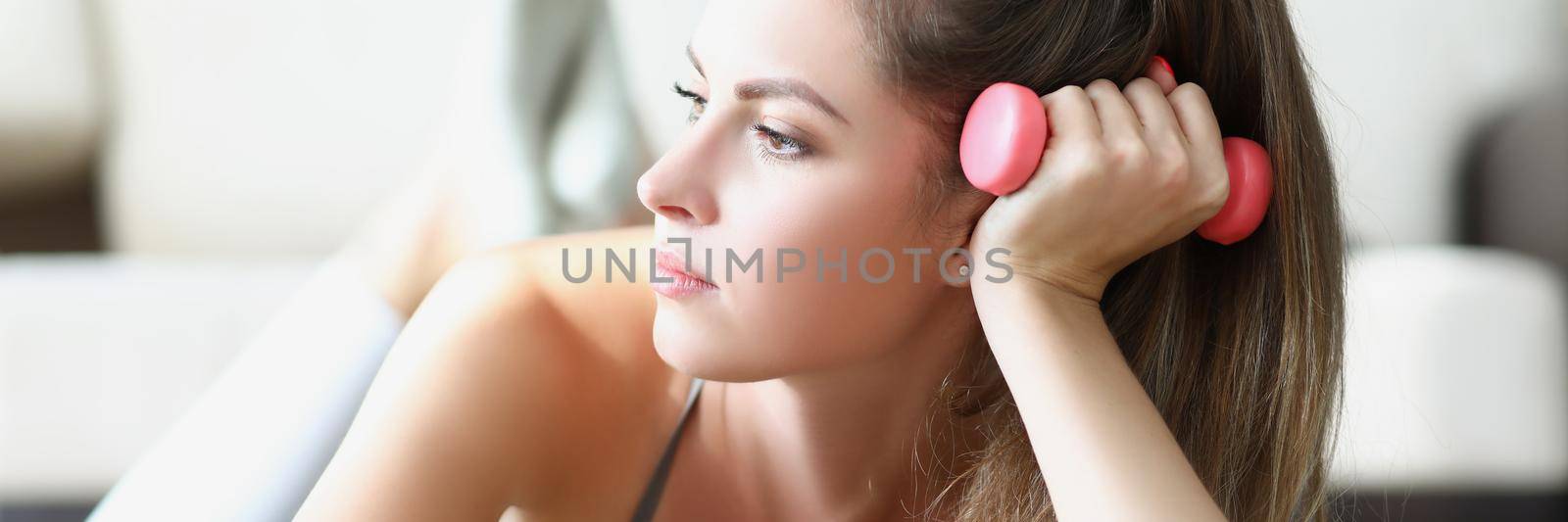 Portrait of young woman taking break between physical exercises laying on carpet. Pretty woman with pink dumbbells tool at home. Sport, weight loss concept