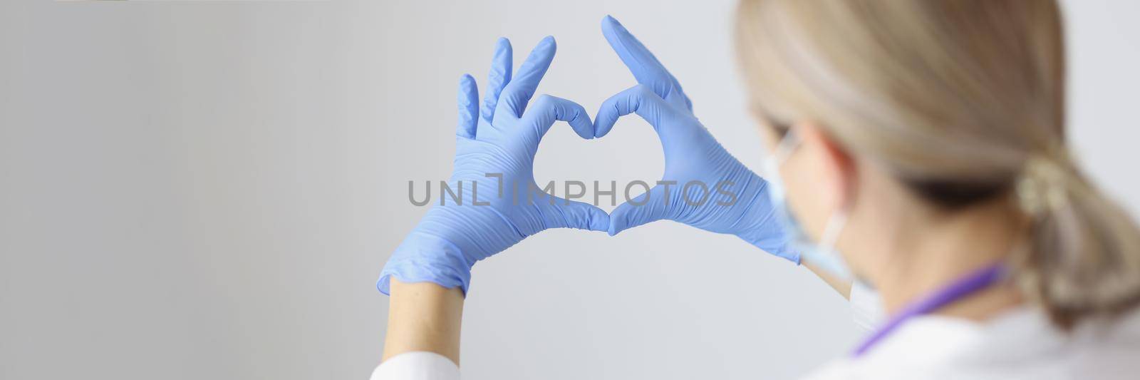 Close-up of medical worker form heart with hands wearing protective gloves. Nurse on day shift in hospital express support for patients. Medicine concept