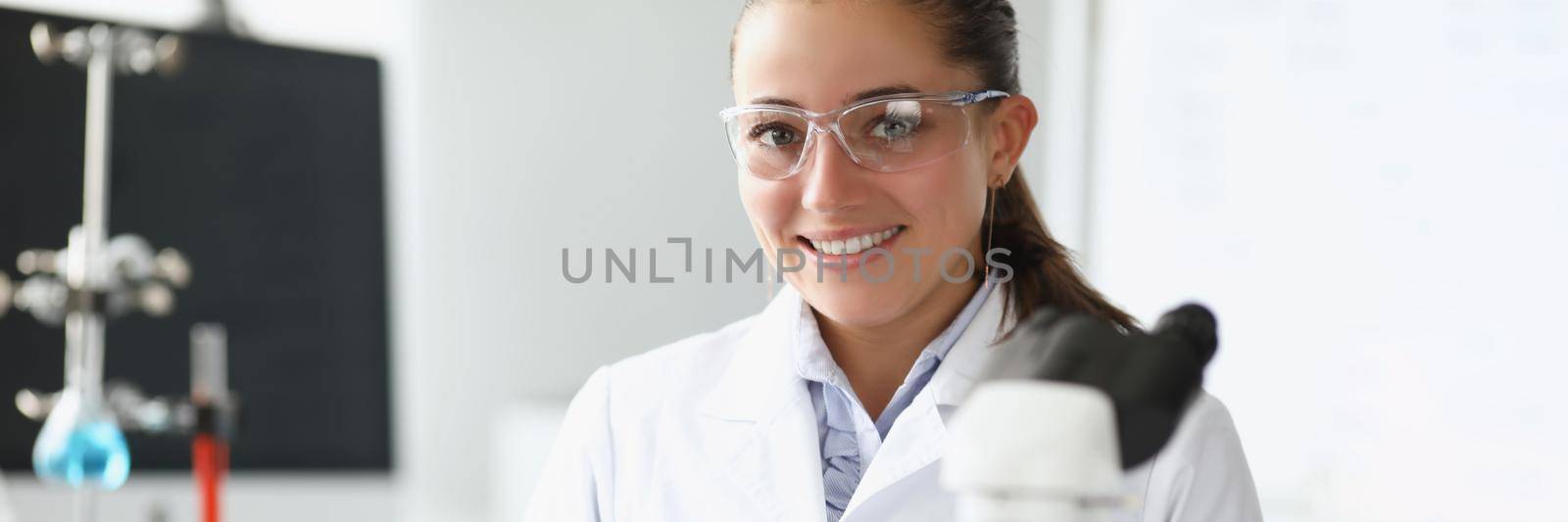 Pretty cheerful laboratory worker in medical gown examine sample under microscope by kuprevich