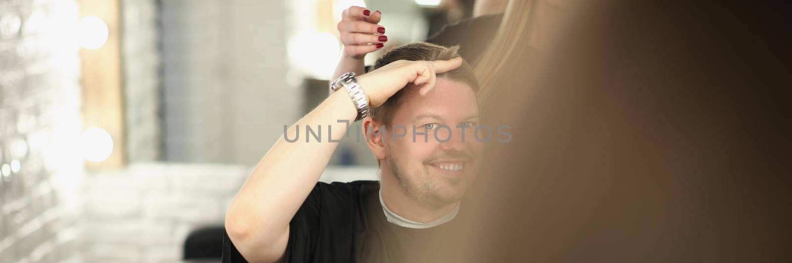 Portrait of middle aged man client show how short he wants his hair cut. Happy person in hairdresser seat waits for new image. Barbershop, hair concept