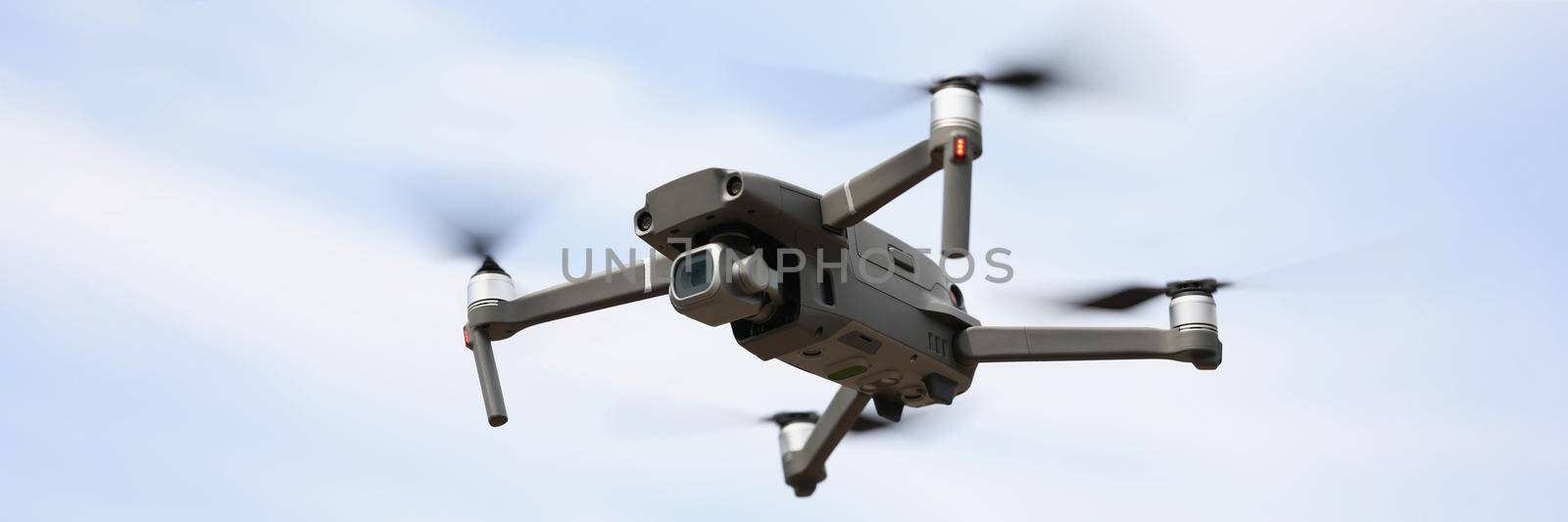 Close-up of modern drone device with remote controller fly and filming in air. Drone flying on blue sky. Digital camera, modern technology, gadget concept