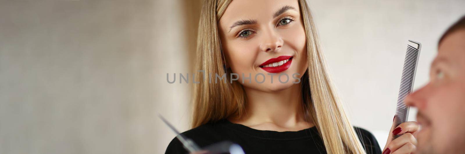 Portrait of young pretty professional master holding tools for work and posing. Middle aged man on hairdresser appointment. Beauty studio, barber concept