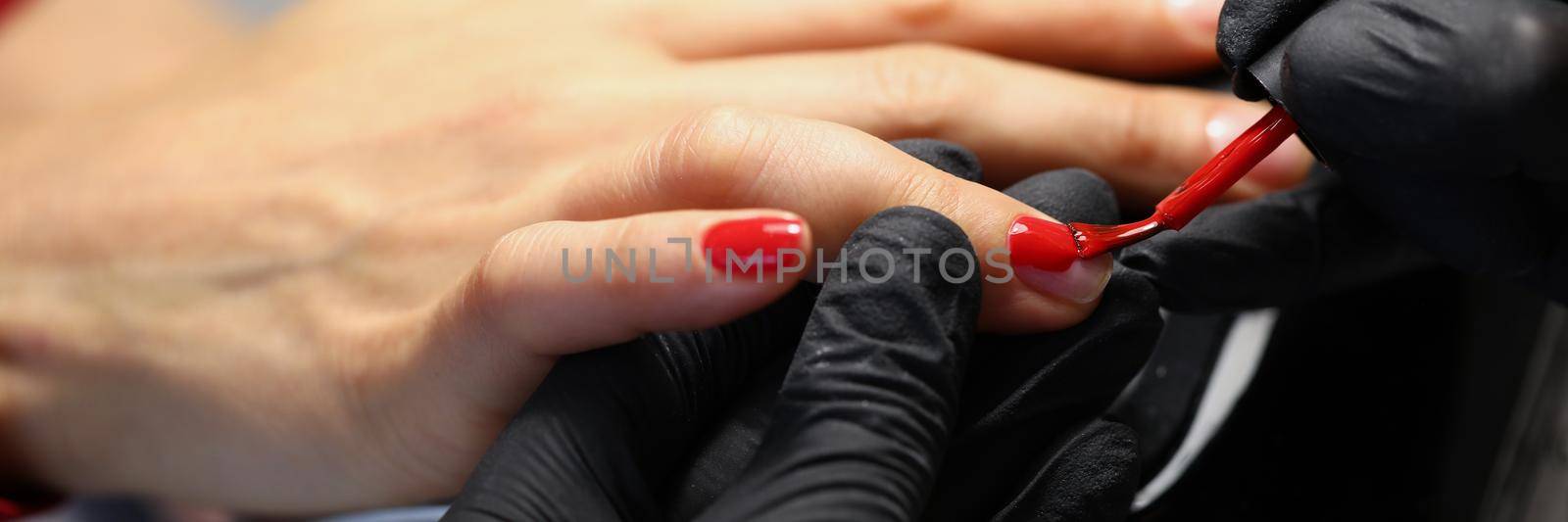 Close-up of professional salon worker cover clients nails with red colour polish. Refresh manicure at luxury beauty centre. Wellness, care, beauty concept