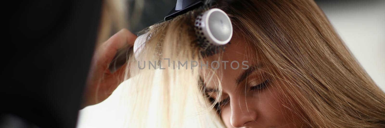 Portrait of blonde woman on planned hairdresser appointment get her hair done with hairdryer. Preparations for date or party. Beauty salon, barber concept