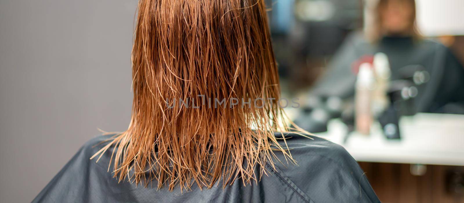 Back view of beautiful wet long red straight hair of young woman in hair salon