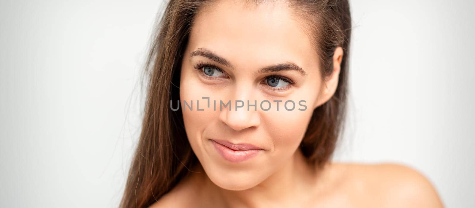 Face portrait of young caucasian woman with naked shoulders and natural make up on white background